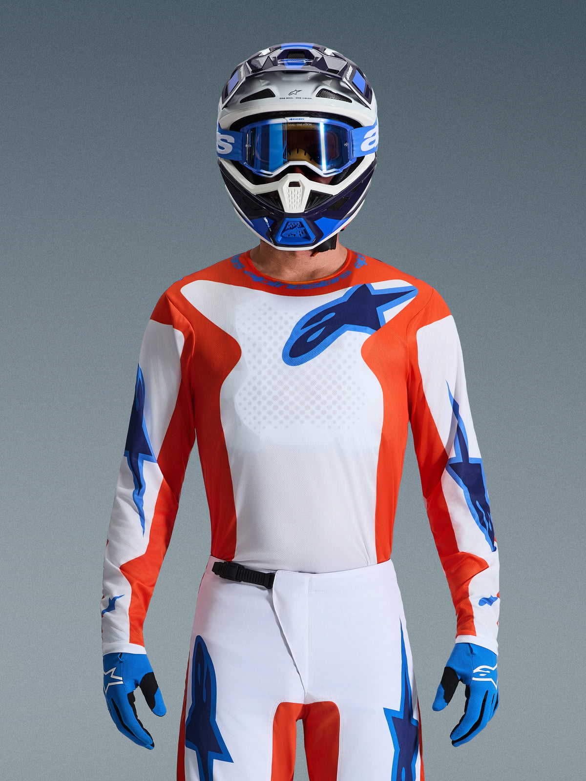 Alpinestars 2026 Fluid Grid Gear Set, motocross-kører iført orange og hvid trøje med blå stjernelogoer, hvide bukser med blå detaljer, matchende blå og hvid hjelm med blå briller og handsker, komplet off-road racingudstyr