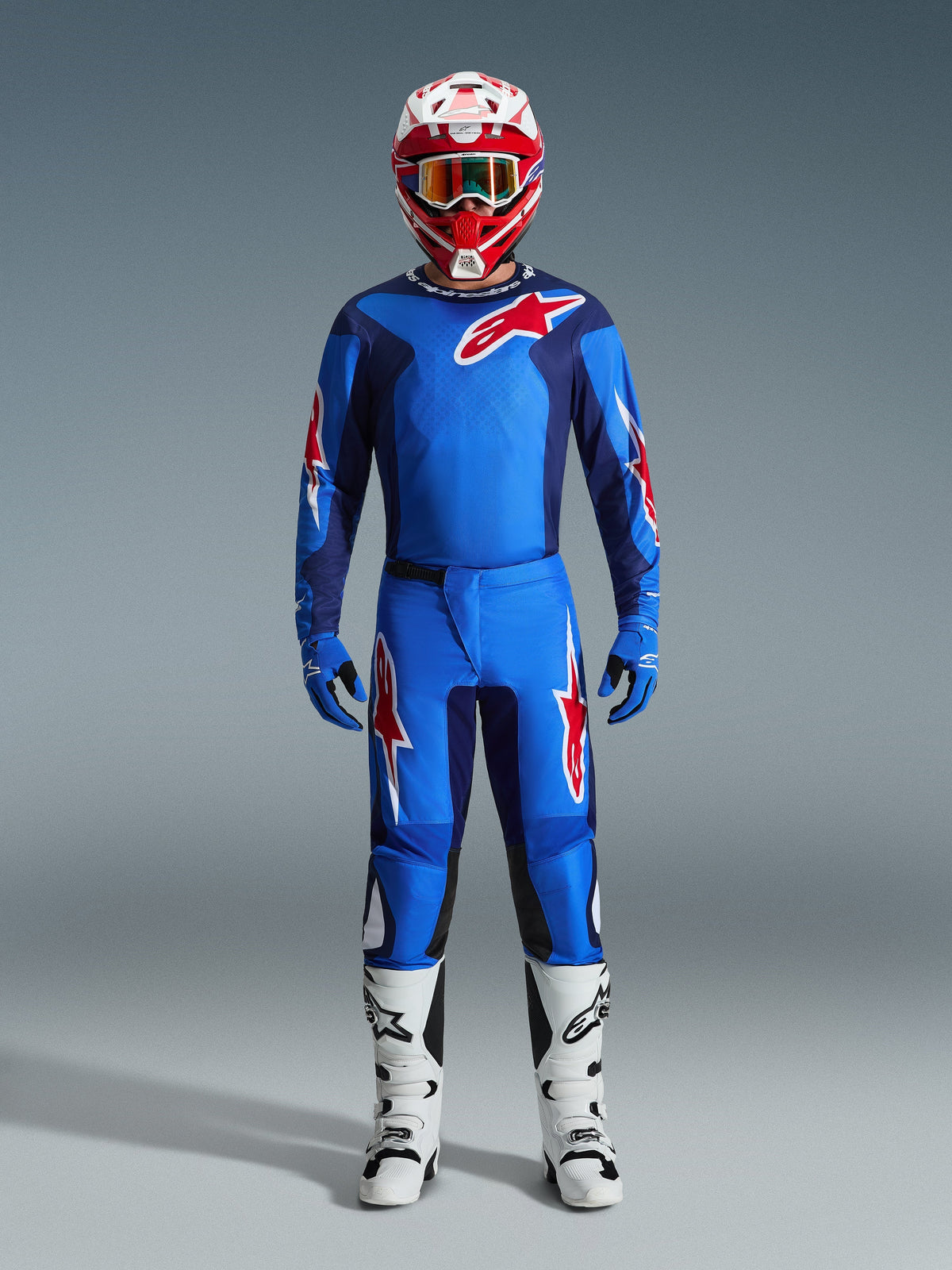 Motocross rider wearing the Alpinestars 2026 Fluid Grid Jersey in Blue and Red, matching blue pants with white and red star logos, red and white helmet with mirrored goggles, blue gloves, and white and black racing boots, complete off-road gear set.
