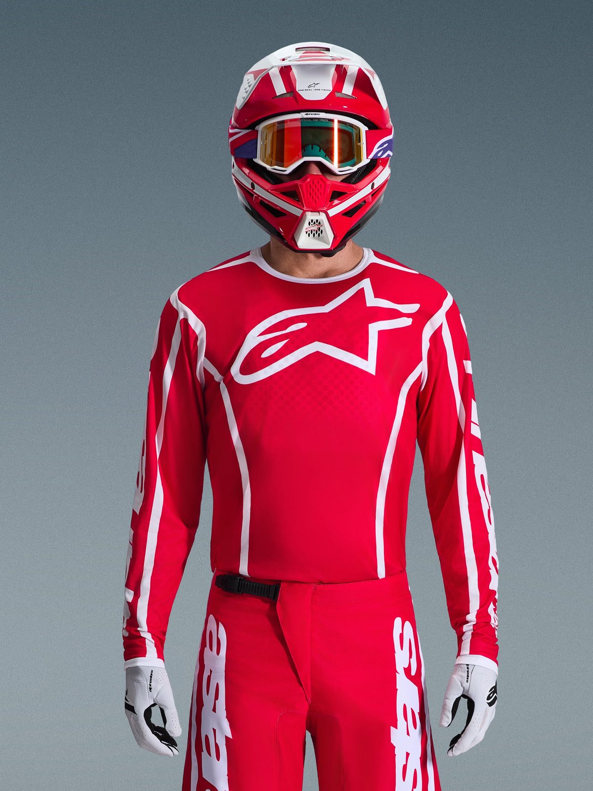 Motocross rider wearing complete Alpinestars 2026 Fluid Apex Gear Set, red jersey with large white star logo on the chest, matching red pants with white branding, red and white helmet with iridescent goggles, white and black gloves, coordinated red and white outfit for off-road racing