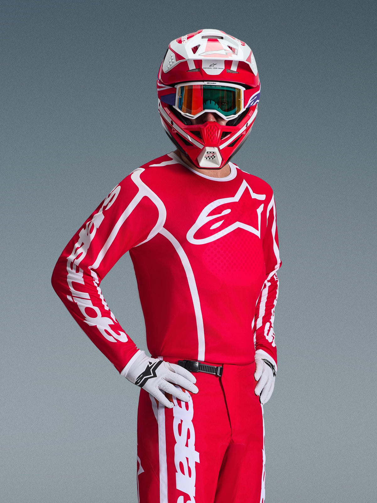 Motocross rider wearing the Alpinestars 2026 Fluid Apex Gear Set in Red and White, featuring a red jersey with white logos, matching pants, white gloves, and a red and white helmet with iridescent goggles, coordinated off-road racing outfit