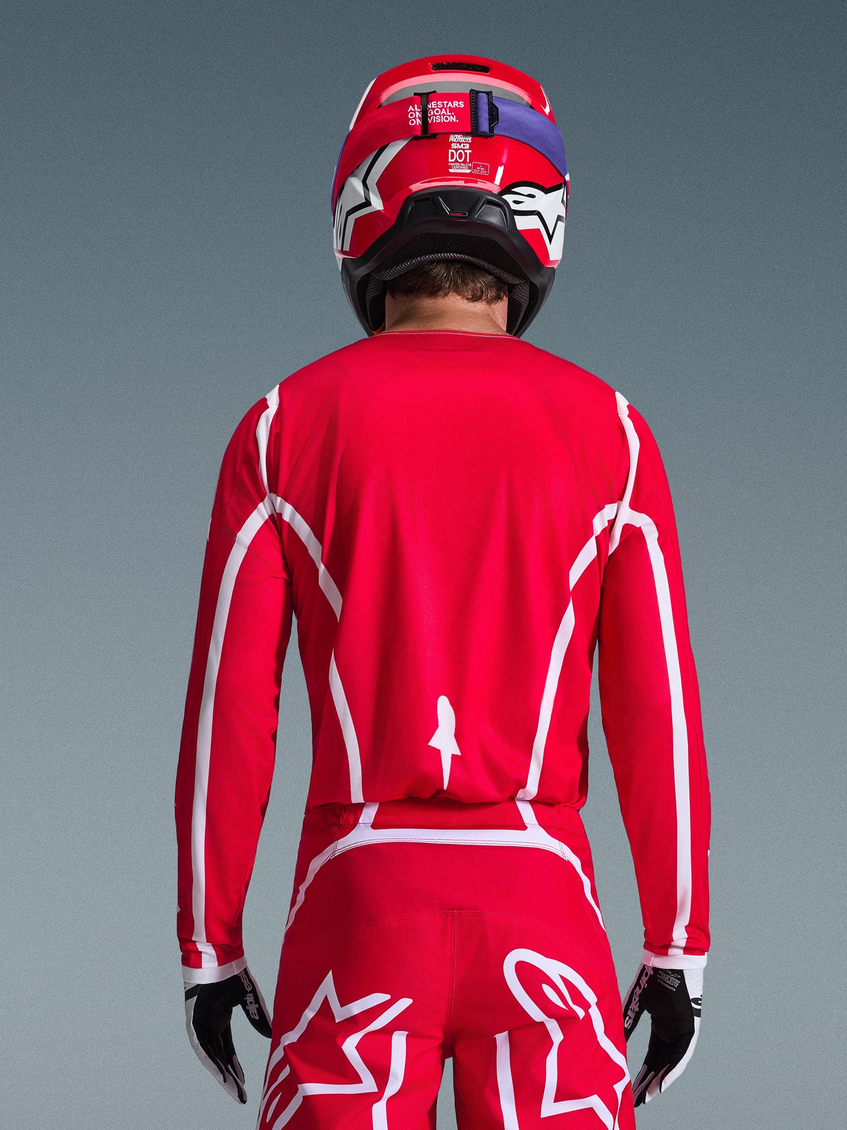 Alpinestars 2026 Fluid Apex-trøje, rød og hvid, set bagfra på en motocross-kører, geometriske hvide mønstre, matchende motocross-bukser og rød hjelm, komplet racerudstyr til off-road-kørsel.