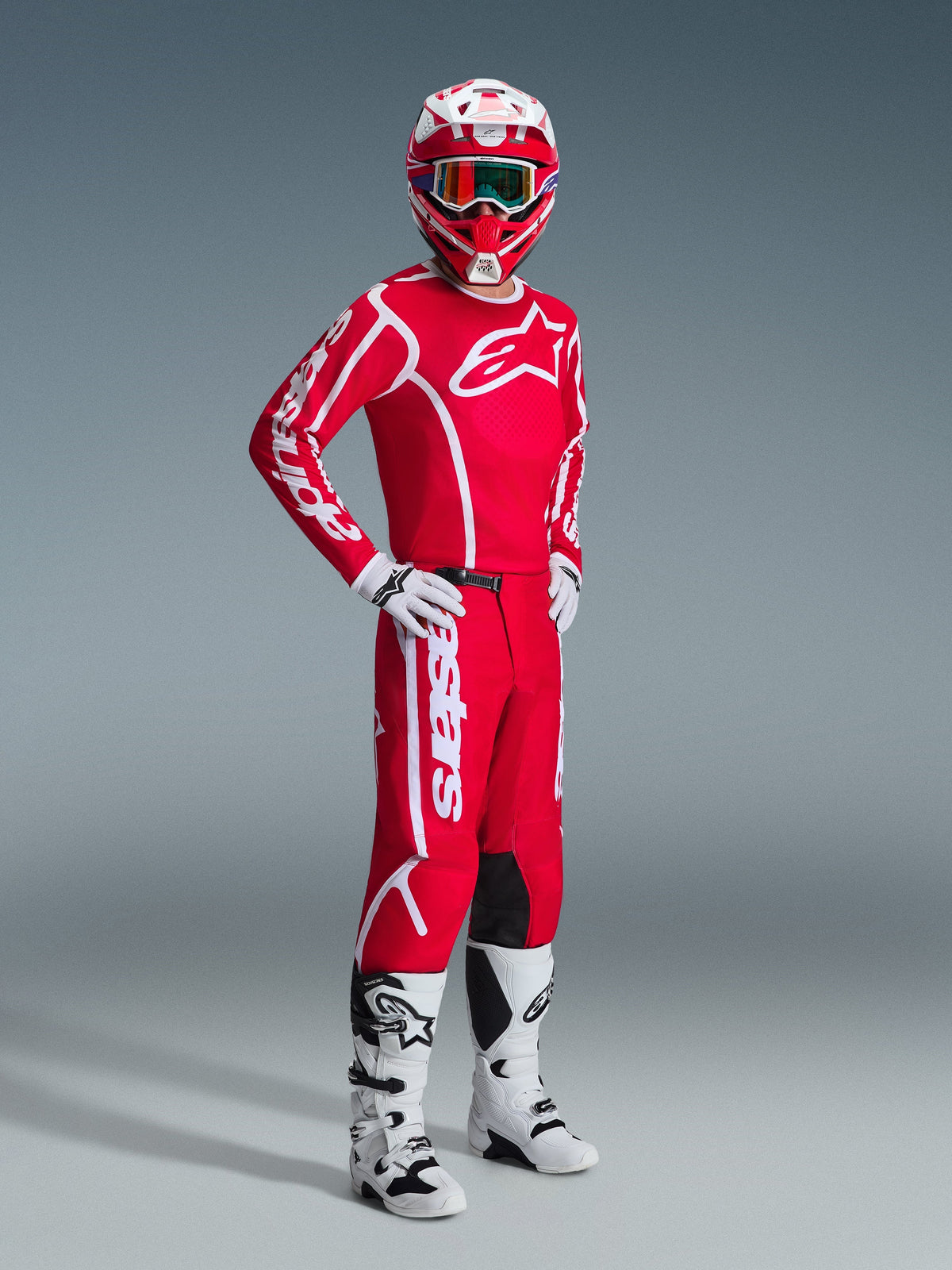 Motocross-kører iført komplet Alpinestars racing-udstyr, herunder 2026 Fluid Apex-trøjen i rød og hvid, matchende røde bukser med hvid branding, rød og hvid hjelm med goggles, hvide og sorte motocross-støvler og hvide handsker, professionelt studiebillede af off-road-udstyr.