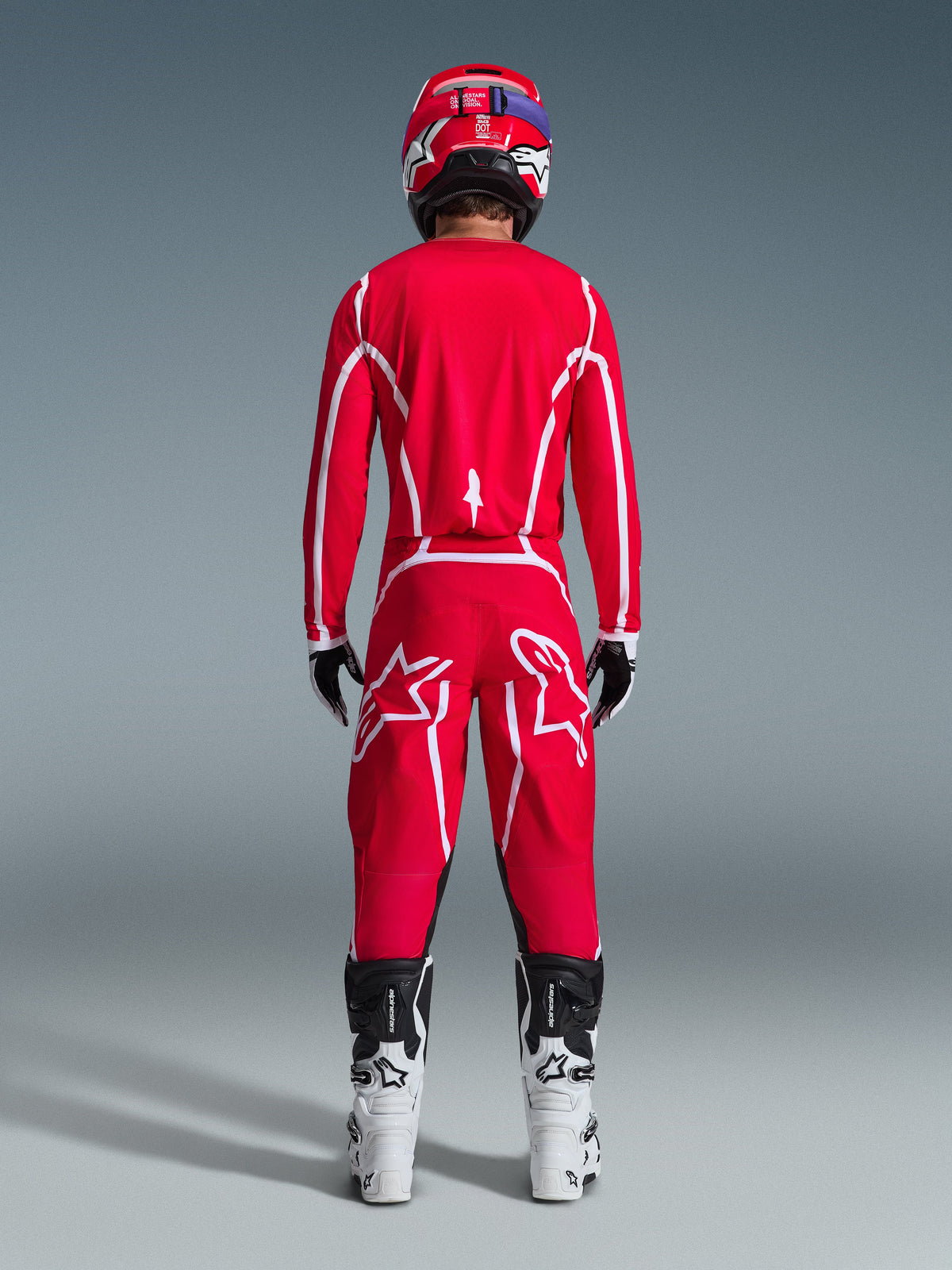 Rear view of a motocross rider wearing the Alpinestars 2026 Fluid Apex Gear Set, bright red jersey and pants with white stripes and logos, paired with white and black boots and a red helmet, professional off-road racing kit