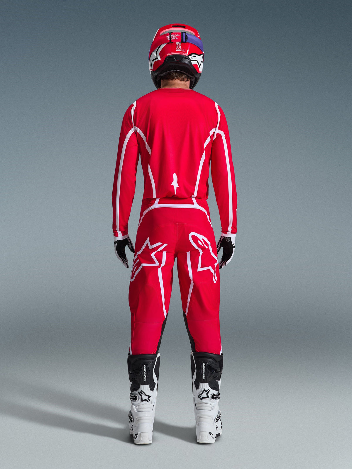 Motocross-kører set bagfra iført Alpinestars 2026 Fluid Apex-trøje i rød og hvid, matchende røde bukser med markante hvide stjernelogoer, en rød hjelm, hvide og sorte motocross-støvler og sort-hvide handsker, komplet udstyr til off-road-kørsel