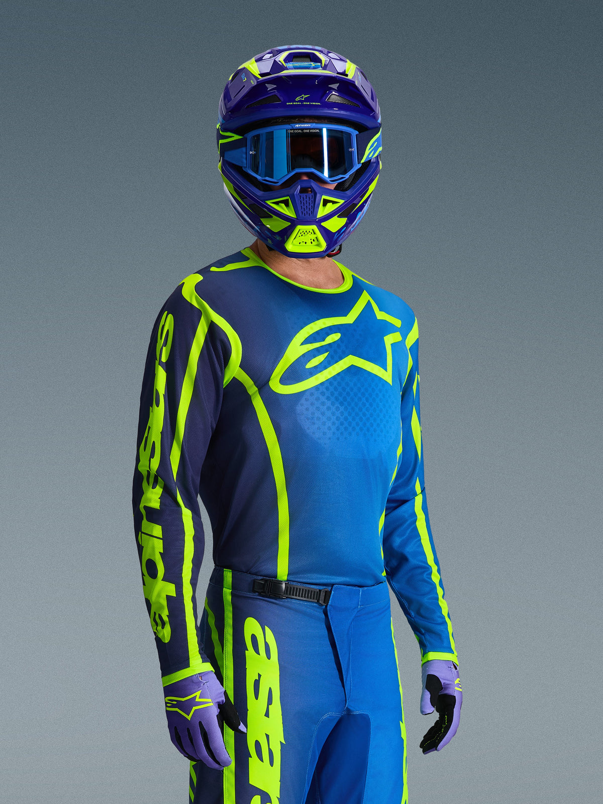 Motocross-kører iført Alpinestars 2026 Fluid Apex Jersey i Blue Yellow Fluo, matchende blå og neongule bukser, lilla og gul hjelm med blå goggles og koordinerede handsker, komplet off-road racerudstyr