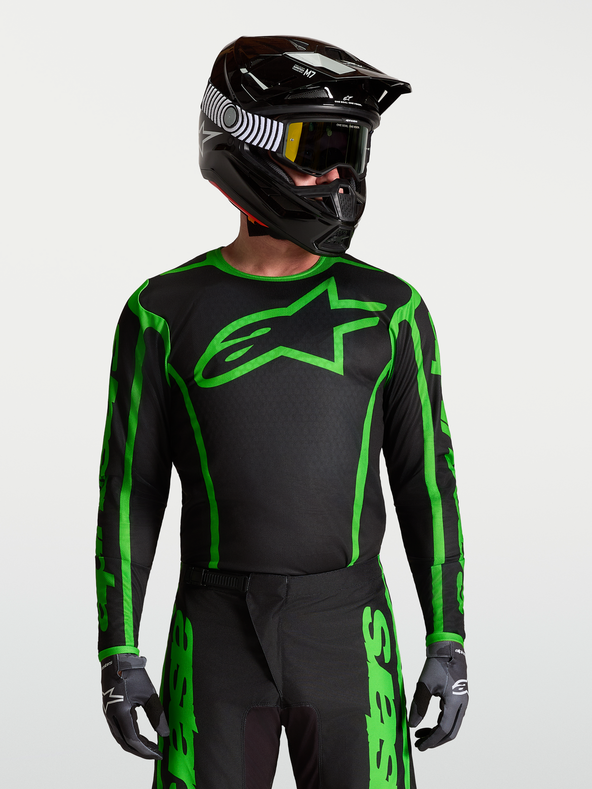 Alpinestars Fluid Apex V2 Jersey, Black and Green Fluo motocross top with moisture-wicking polyfabric on model with helmet.