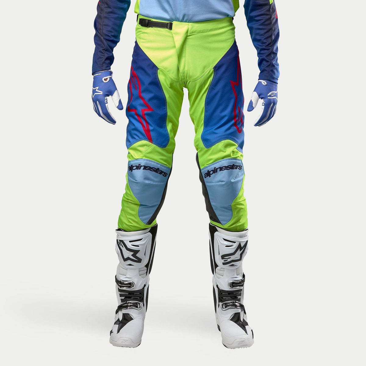 Alpinestars 2024 Racer Hoen bukser, motocrossbukser, gul fluo og mørkeblå, vist med hvide og sorte motocrossstøvler og blå handsker, med markante røde logoer, lyseblå knæpaneler og et sportsligt ergonomisk design til off-road kørsel