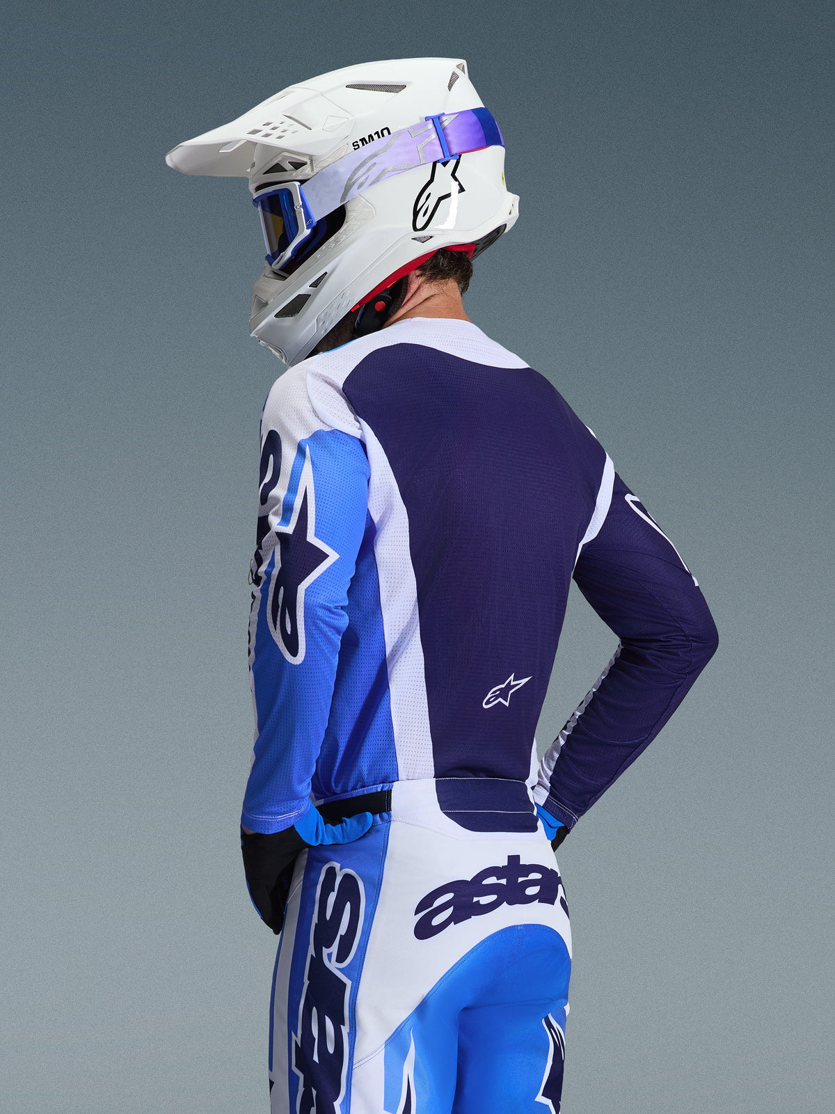 Motocrosskører iført Alpinestars 2026 Racer Air Portl trøje i Ucla Blue og hvid, set bagfra med fokus på det åndbare mørkeblå mesh-rygpanel, båret med matchende bukser og en hvid Alpinestars-hjelm med blå briller, koordineret motocross-udstyrssæt.