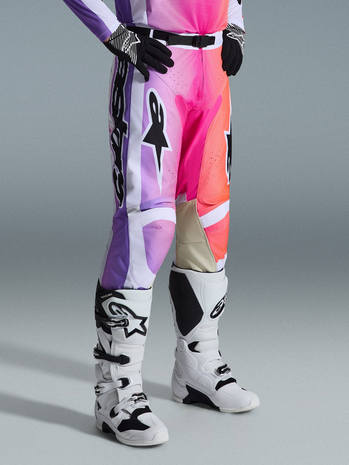 Alpinestars 2026 Racer Air Portl bukser, motocrossbukser, flerfarvet grafik med lilla, pink og orange farveovergange, båret med hvide og sorte motocrossstøvler og sorte handsker, med race fit-design og beige læderpaneler på indersiden af knæene