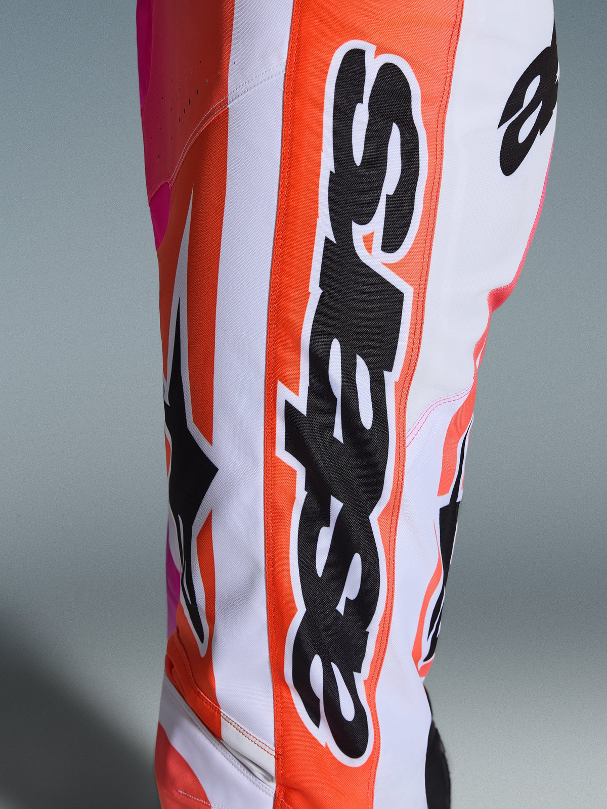 Alpinestars 2026 Racer Air Portl bukser, motocross-bukser, orange, hvid og pink, nærbillede der viser stort sort Alpinestars-branding og stjernelogo, perforeret stof til ventilation, slidstærkt racerudstyr til off-road
