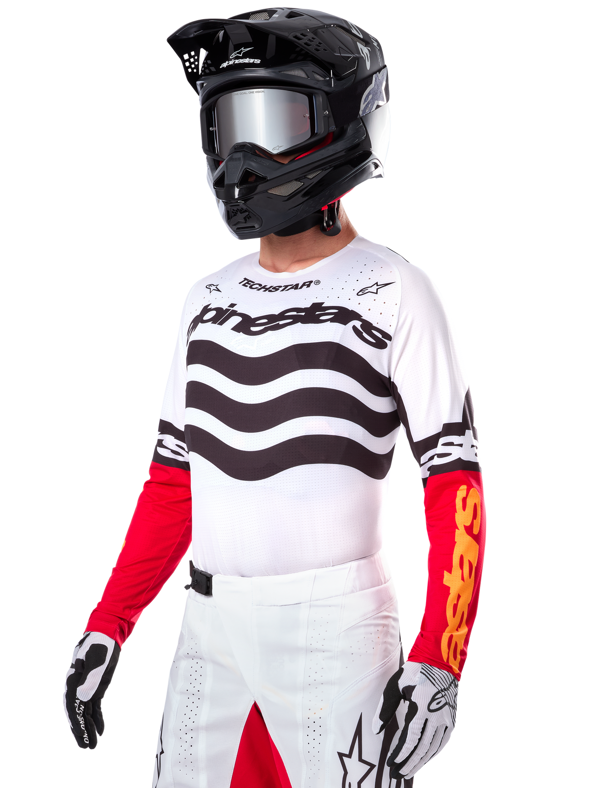 Motocross-kører iført Alpinestars Limited Edition Techstar Deep Jersey, hvid trøje med sorte bølgeformede striber og røde underærmer, kombineret med en sort hjelm, spejlede goggles, hvide og sorte handsker og hvide racing-bukser, funktionelt motocross-outfit.