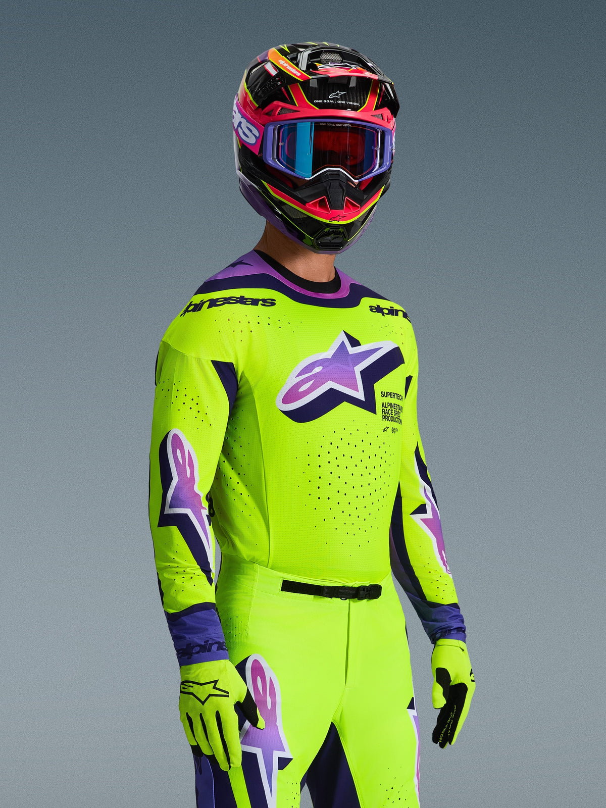Alpinestars 2026 Supertech Vista Jersey og matchende udstyrssæt, motocross-kører i klar gul med lilla og sorte detaljer, stort lilla Astar-logo på brystet og ærmerne, matchende handsker og flerfarvet racerhjelm med goggles, atletisk pro-niveau pasform til terrænkørsel