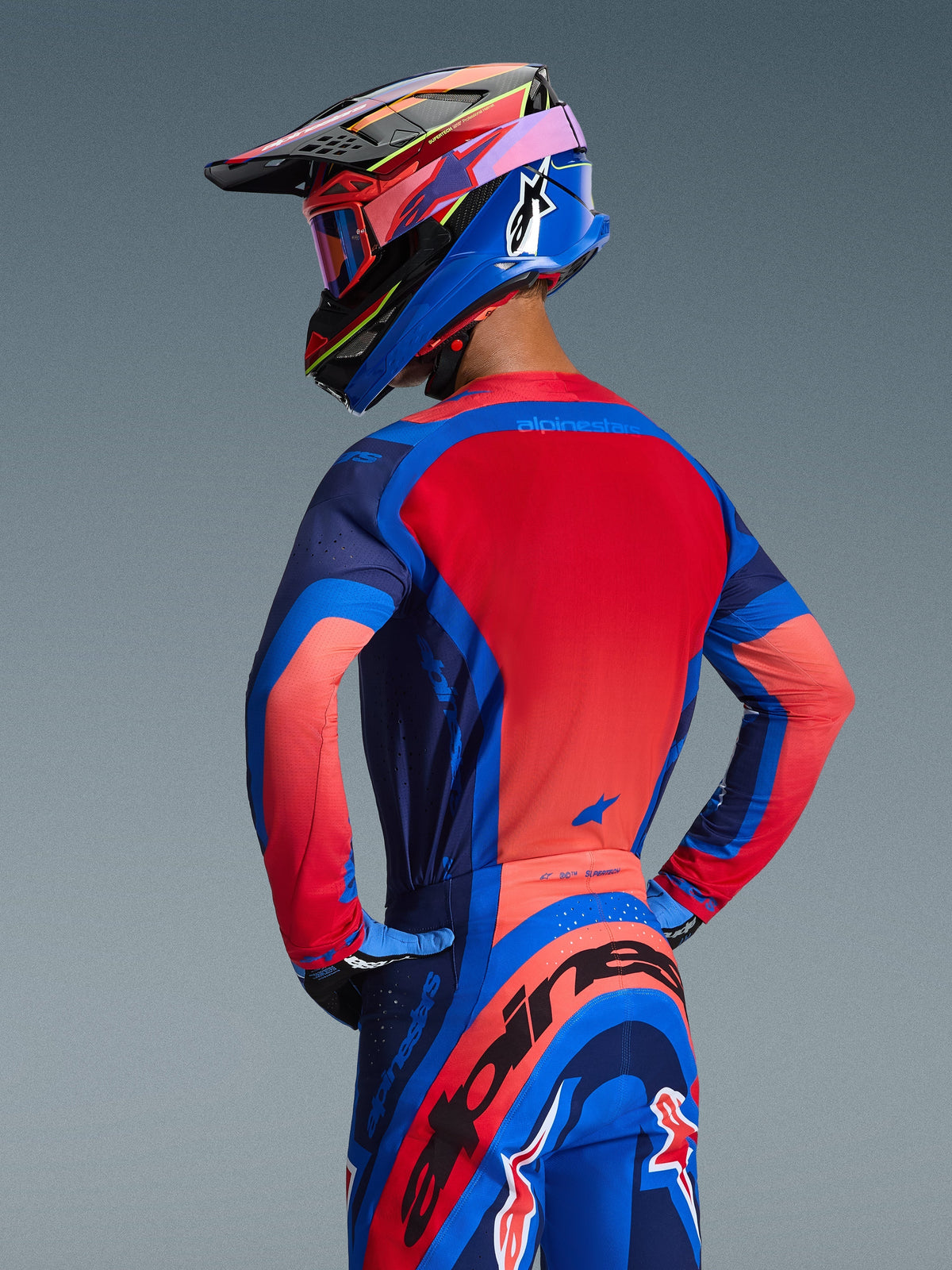 Alpinestars 2026 Supertech Vista udstyrssæt, motocross-trøje og -bukser i Dark Navy, Hot Coral og Cobalt, set bagfra af en kører iført en matchende multifarvet hjelm og goggles, atletisk race-fit racerbeklædning