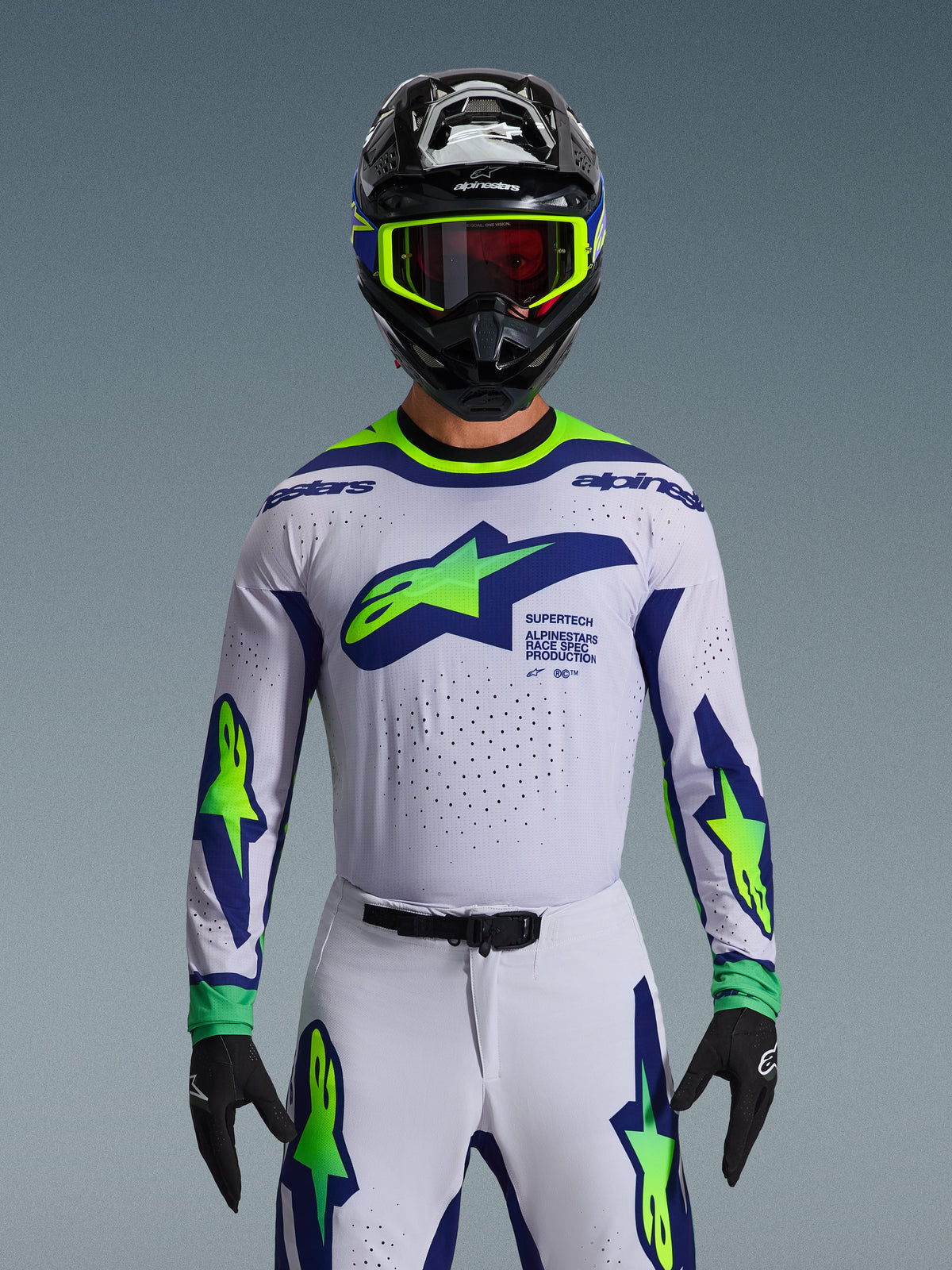 Alpinestars 2026 Supertech Vista udstyrssæt, motocross jersey og bukser, hvid med blå og neongrøn grafik, båret med sort hjelm og neongrønne goggles, med laserskåret ventilation og atletisk race-pasform til professionel racing.