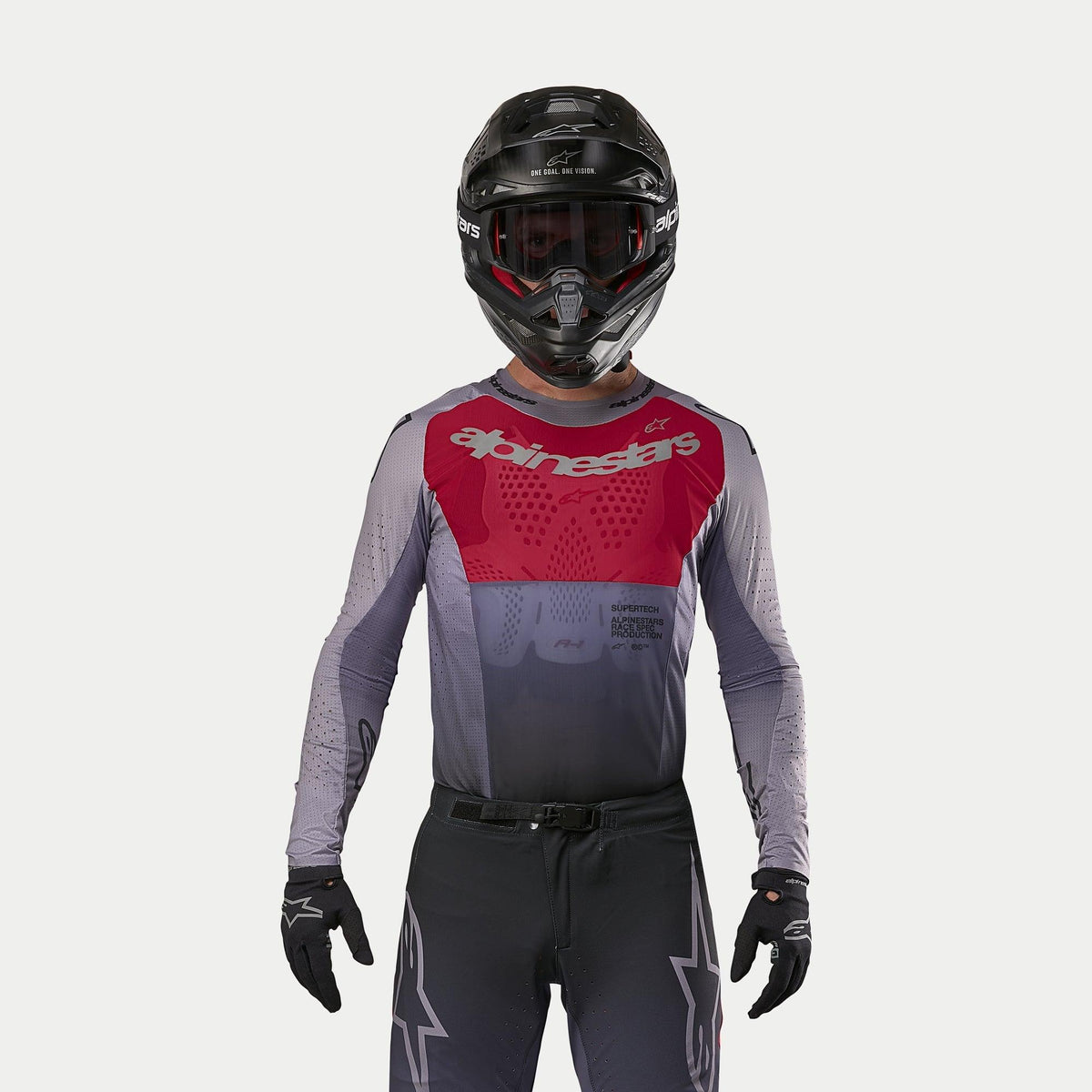 Motocross-kører iført Alpinestars 2024 Supertech Dade-trøje i Iron Red Berry, med rødt brystpanel og grå ærmer med sølvbranding, båret med matchende bukser, sort hjelm og sorte handsker, professionelt off-road racerudstyr