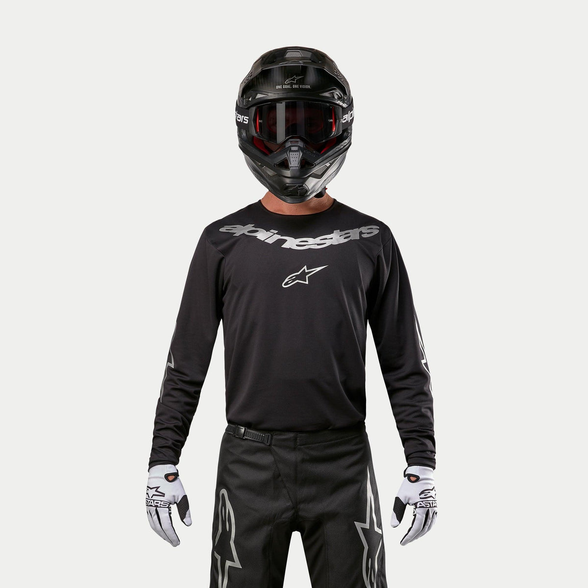 Alpinestars 2024 Fluid Graphite trøje, sort og sølv motocross-jersey, båret af en kører med sort hjelm og røde briller, med sølvfarvet Alpinestars-branding på brystet, koordineret med sorte bukser og hvide handsker til terrænkørsel