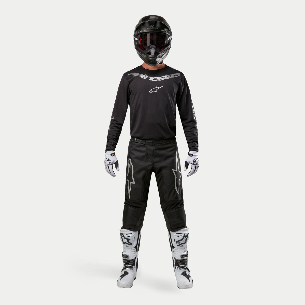 Motocrossrytter iført komplet racerudstyr, Alpinestars 2024 Fluid Graphite-trøje i sort og sølv, sorte bukser med sølvstjerne-logoer, sort hjelm med røde goggles, hvide og sorte støvler, hvide og sorte handsker, koordineret motocross-outfit