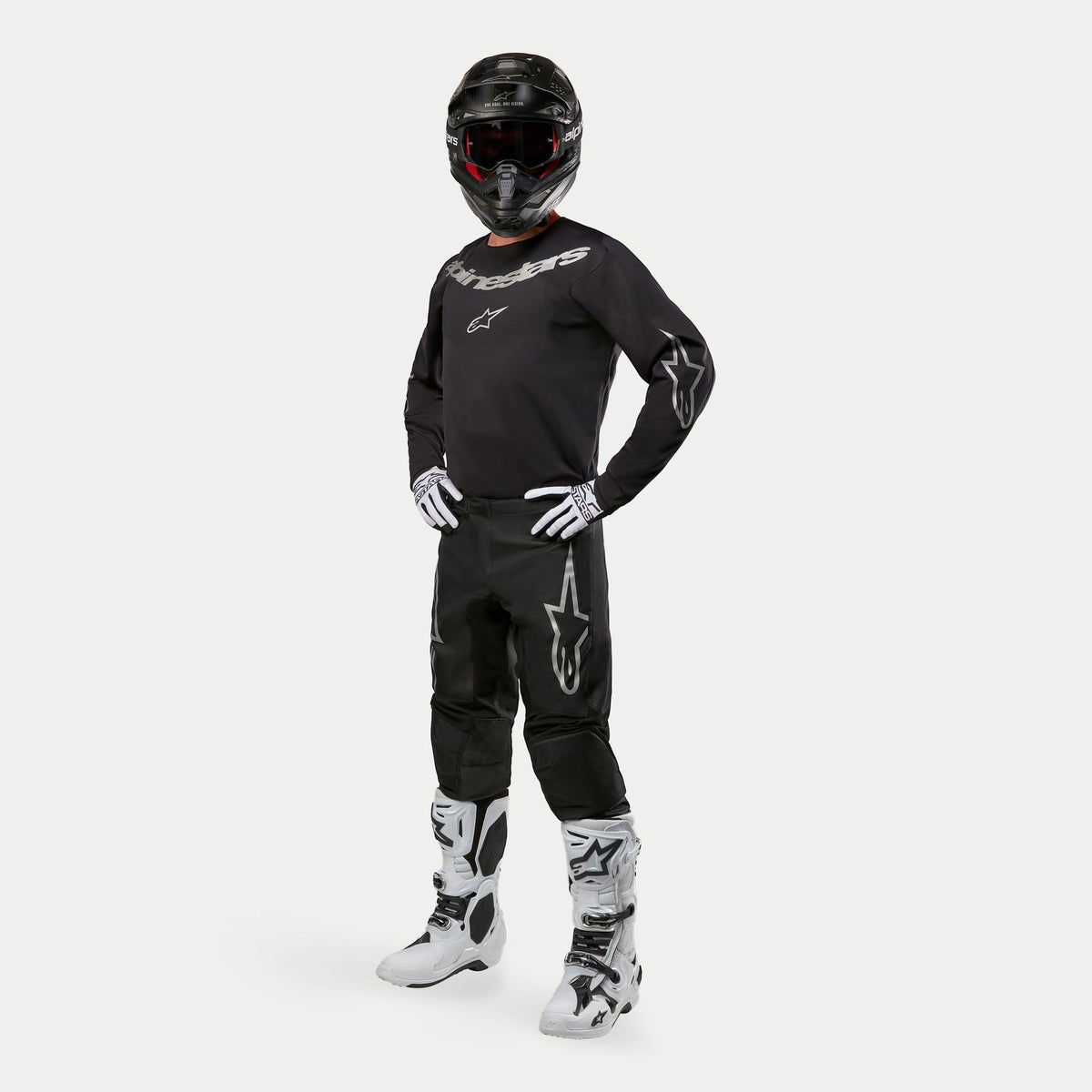 Motocross-rytter iført Alpinestars 2024 Fluid Graphite trøje i sort og sølv, matchende sorte bukser med sølvstjerne-logoer, hvide og sorte støvler, hvide og sorte handsker og en sort hjelm med røde goggles, komplet off-road racerudstyr
