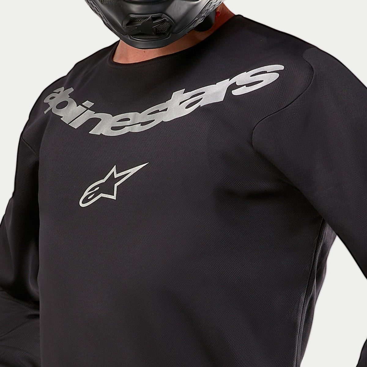 Alpinestars 2024 Fluid Graphite trøje, motocross-trøje, sort og sølv, nærbillede af brystet med sølv Alpinestars-branding og stjerne-logo, åndbar poly-stofkonstruktion, båret af en rytter med sort hjelm
