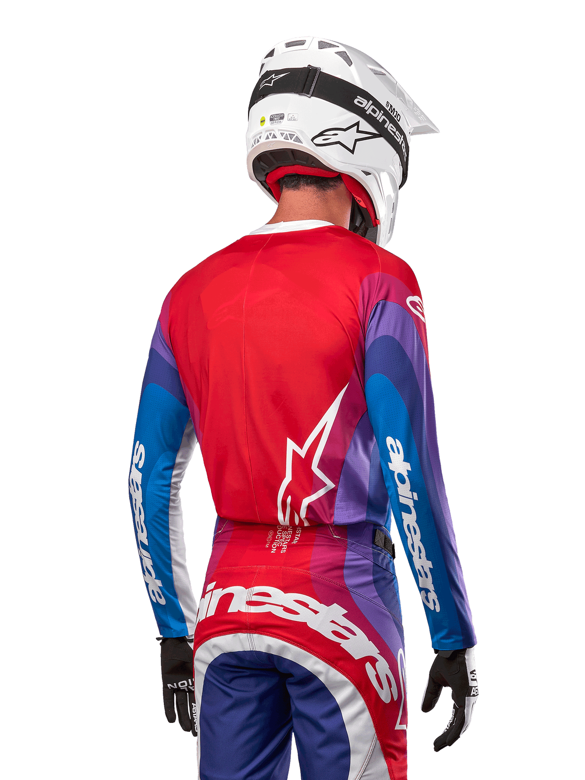Motocross rider from behind wearing Alpinestars 2024 Techstar Pneuma Jersey in Blue Mars Red White, featuring a red back with white star logo, blue and purple sleeves with white branding, coordinated with matching pants and a white helmet for off-road racing.