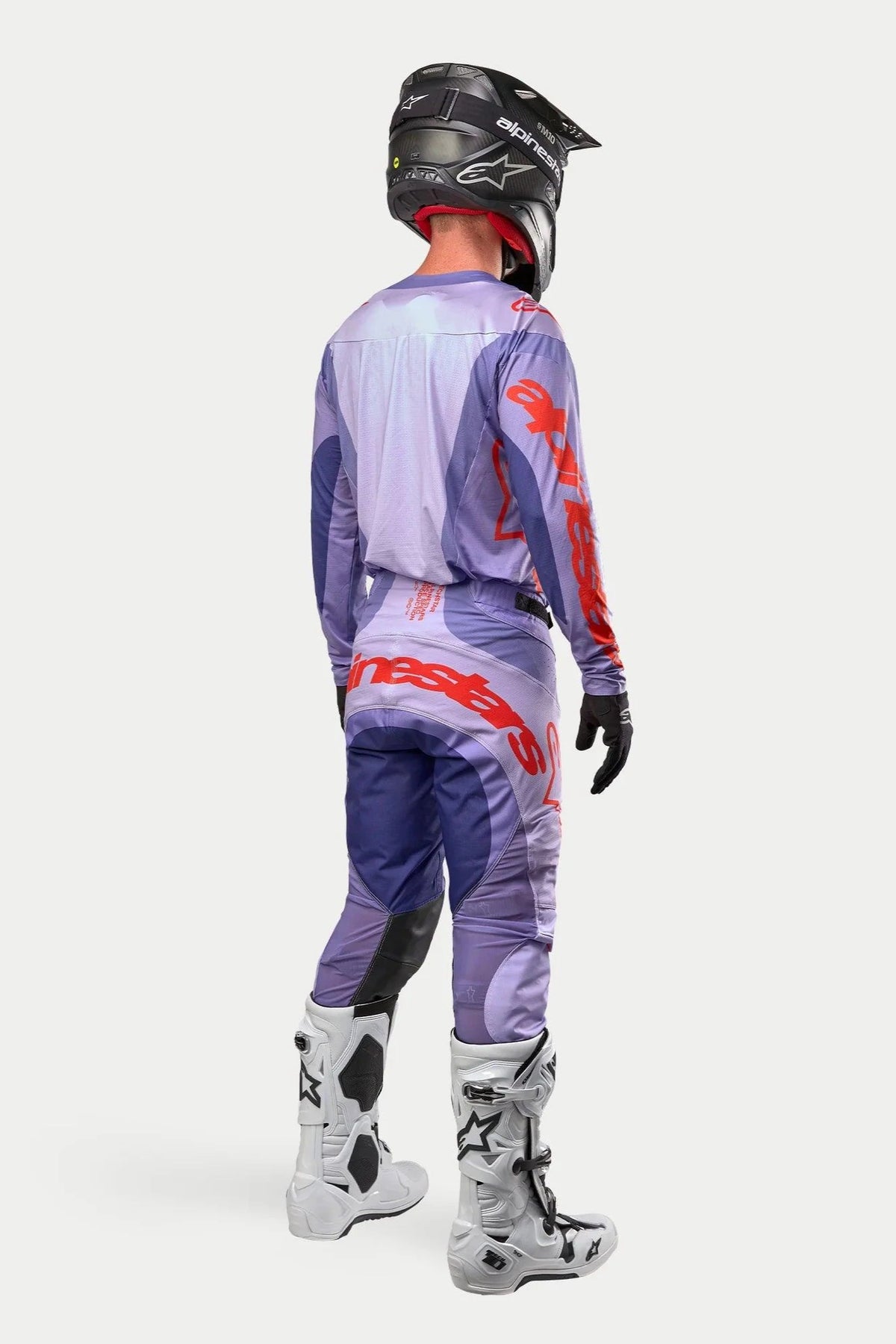 Motocross rider wearing complete racing gear from the rear, Purple Alpinestars 2024 Techstar Ocuri Jersey with hot orange branding, matching purple pants with orange details, black helmet, white and black boots, black gloves, professional off-road racing kit