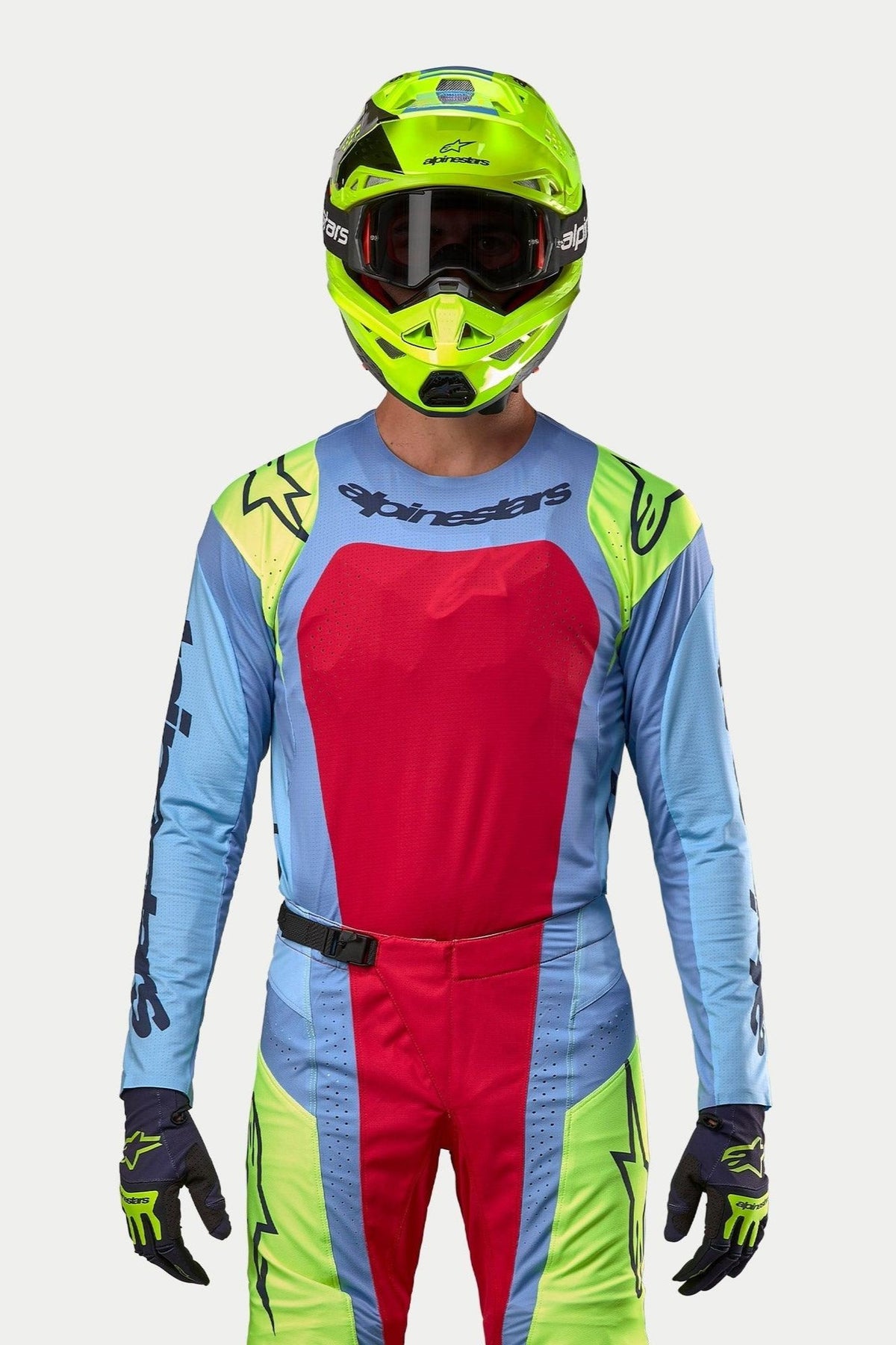 Alpinestars motocross-kører iført komplet racerudstyr, 2024 Techstar Ocuri Jersey i lyseblå med et stort Red Berry-brystpanel og gule fluo-detaljer på skuldrene, matchende fluorescerende gul hjelm, koordinerede røde og gule fluo-bukser, professionelt outfit til off-road racing
