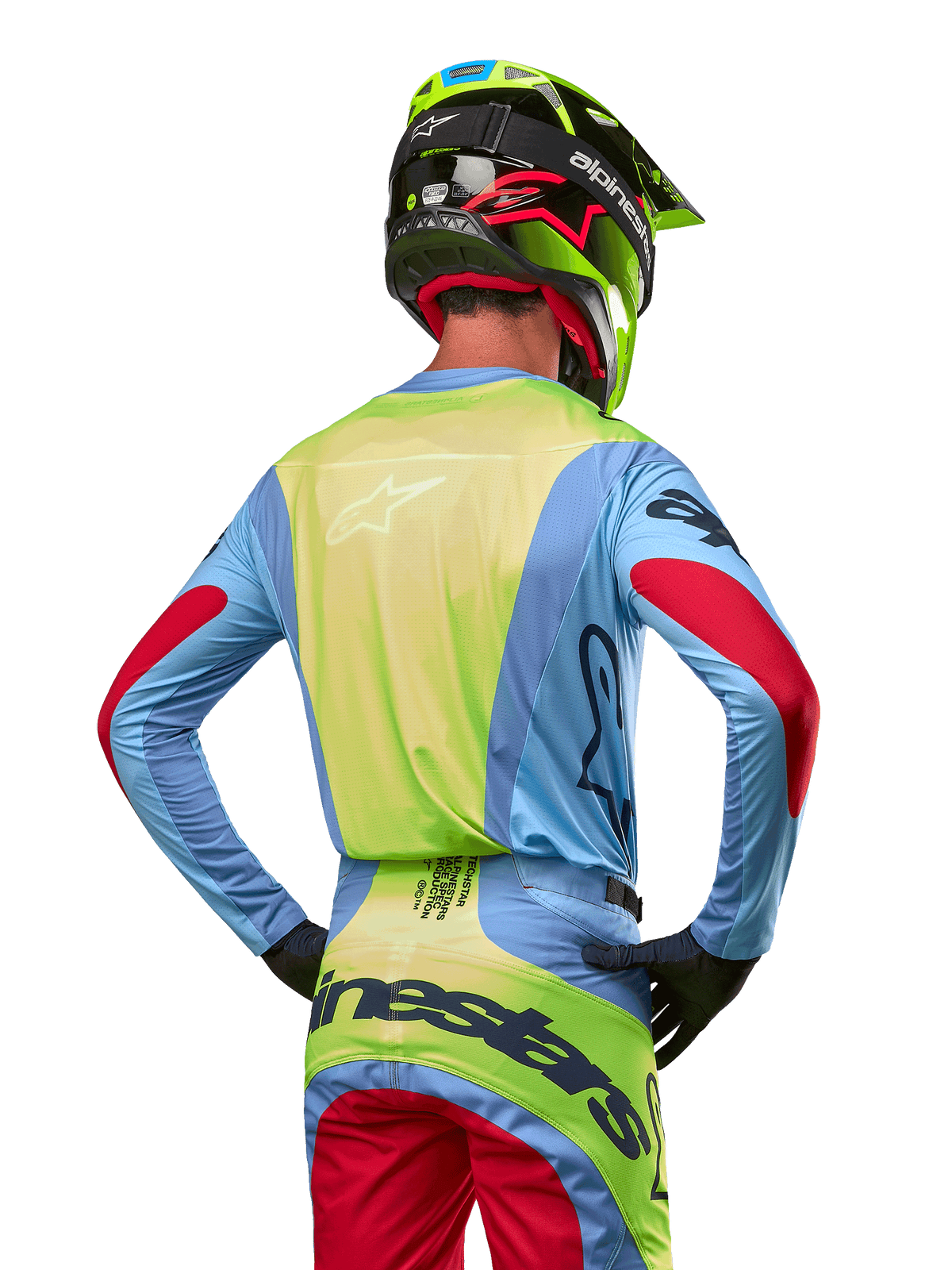 Motocrossrytter set bagfra iført Alpinestars 2024 Techstar Ocuri-trøje, lyseblå med neongul ryg og røde detaljer på ærmerne, matchende motocrossbukser og neongul hjelm, koordineret outfit til off-road kørsel