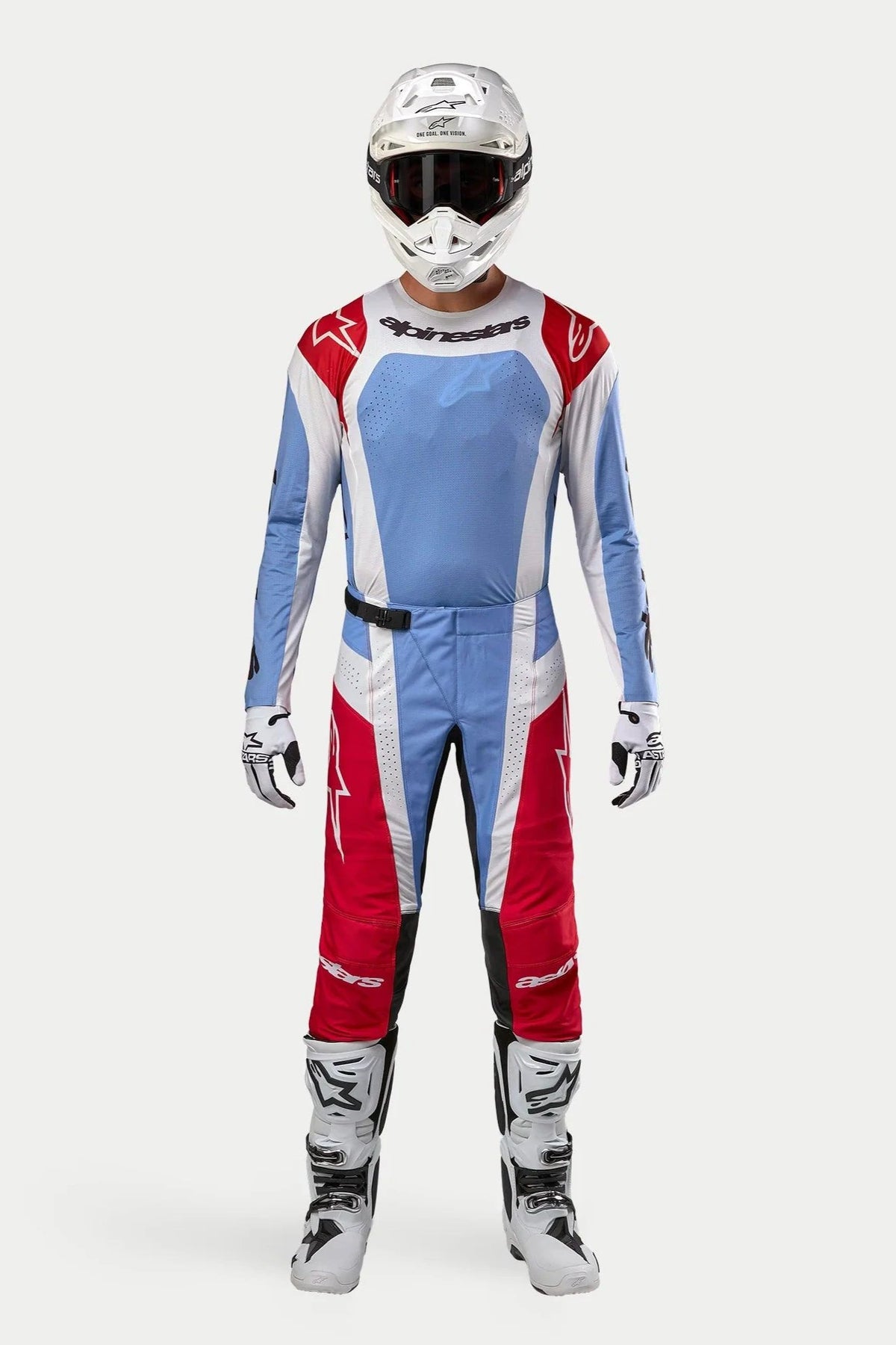 Motocross-kører iført Alpinestars 2024 Techstar Ocuri Jersey i lyseblå, rød og hvid, matchende motocross-bukser, hvid hjelm med goggles og hvide støvler, komplet professionelt off-road racingsæt.