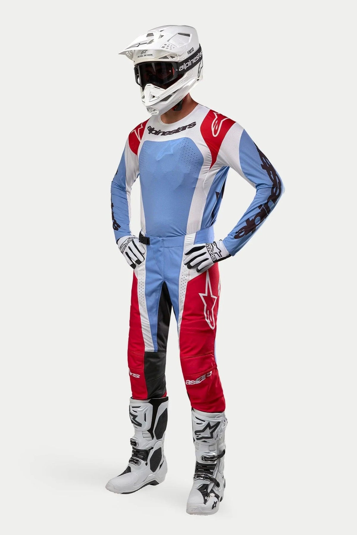 Motocross-kører iført komplet racerudstyr med Alpinestars 2024 Techstar Ocuri Jersey i lyseblå, mars-rød og hvid, matchende bukser, hvid hjelm med goggles, hvide støvler og hvid-sorte handsker.