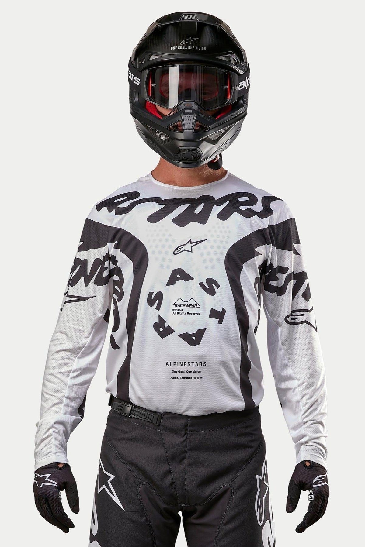 Motocrosskører iført Alpinestars 2024 Racer Hana trøje i hvid og sort, kombineret med en sort hjelm og sorte motocrossbukser, med markant sort 'ASTARS'-grafik og et cirkulært centralt logo, professionelt terrænkørselsudstyr