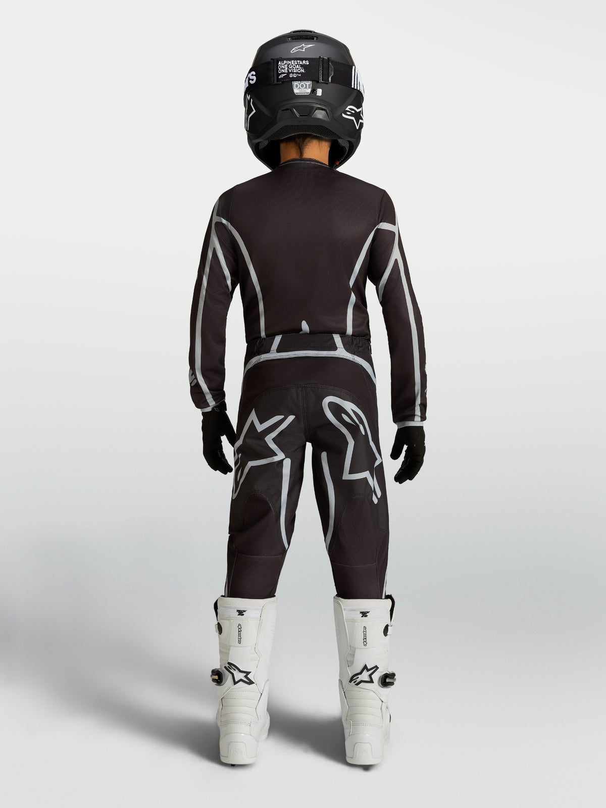 Alpinestars Fluid Apex V2 trøje og udstyrssæt til ungdom, sort og sølv motocross-sæt med hvide støvler, set bagfra.