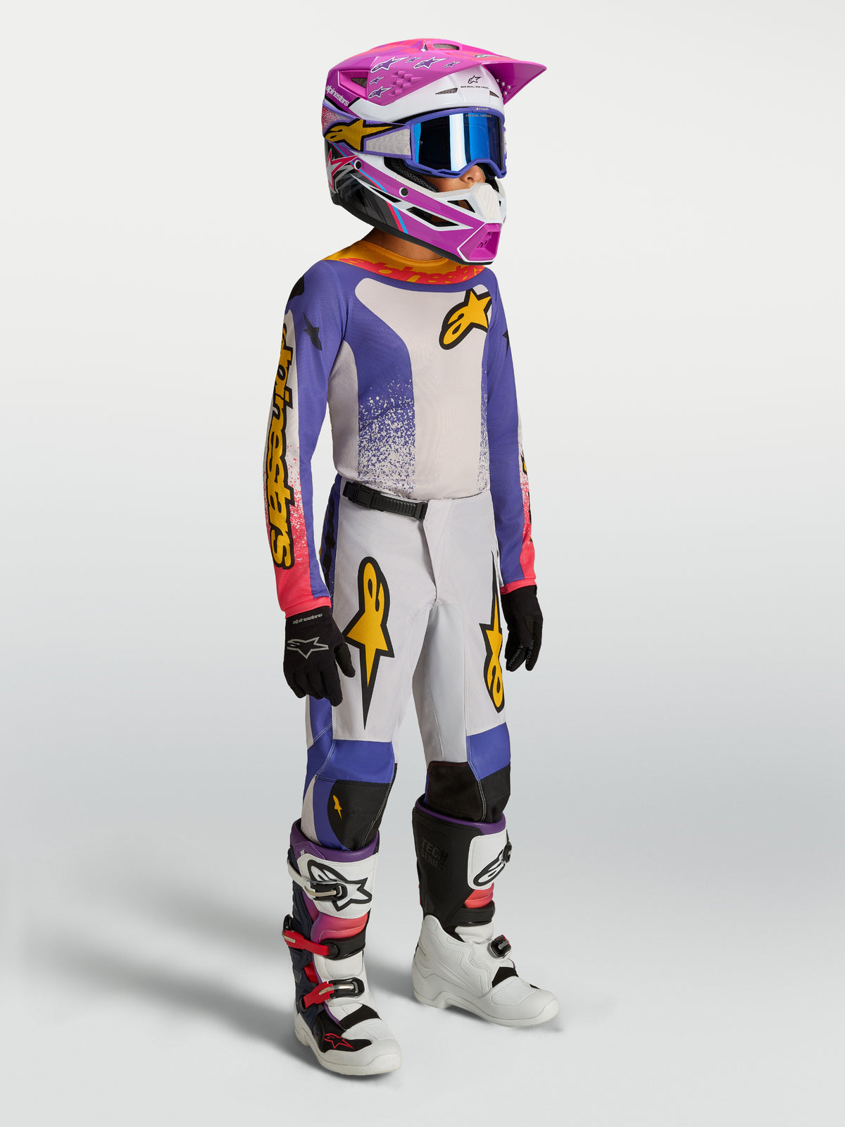 Alpinestars ungdom Fluid Drag udstyrssæt, motocross-racerudstyr i blå og hvid med pink og guld detaljer, vist på model.