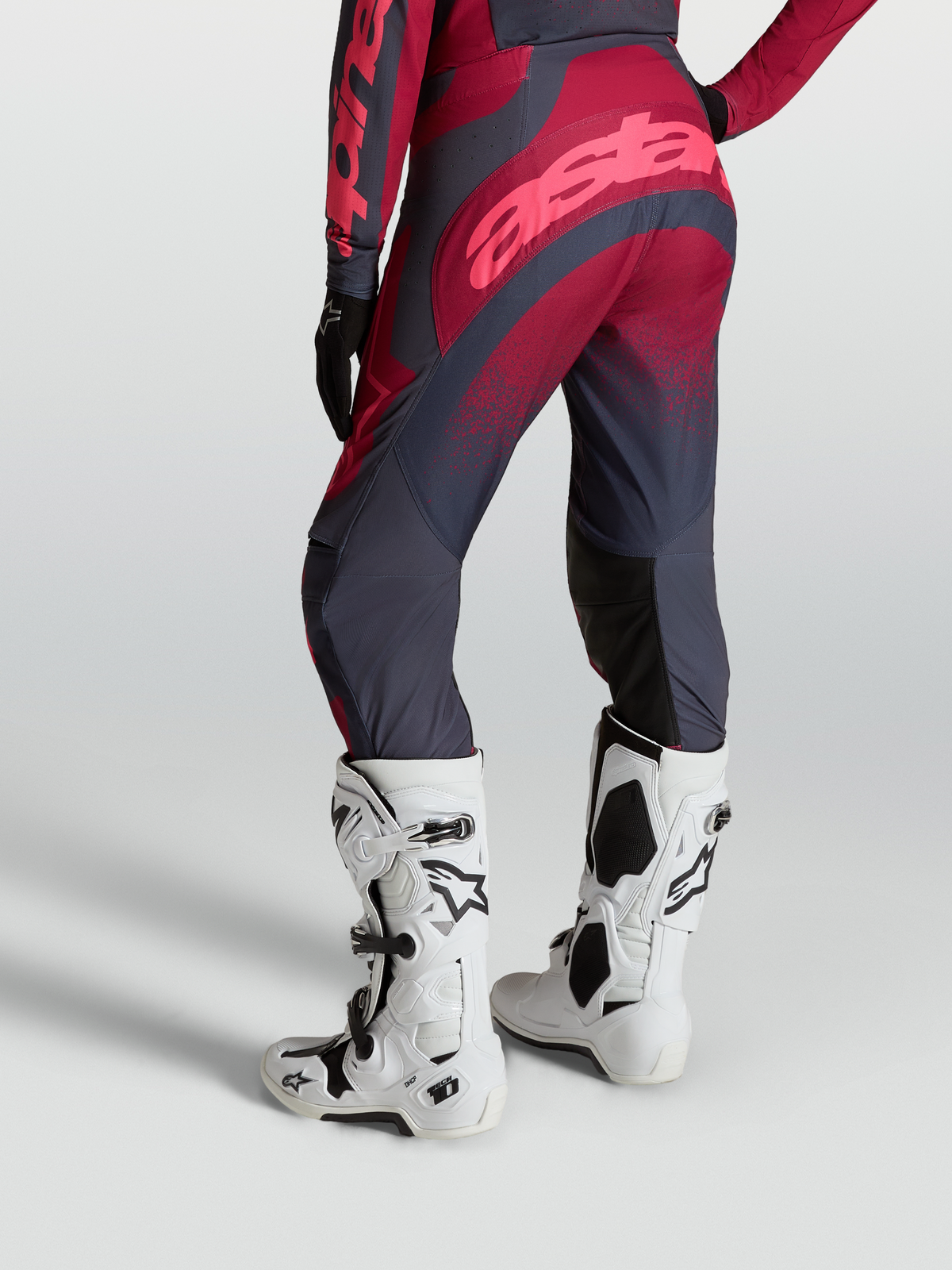 Alpinestars Stella Techstar Swan motocrossbukser til kvinder, grå og rød, set bagfra med hvide Tech 10 støvler.