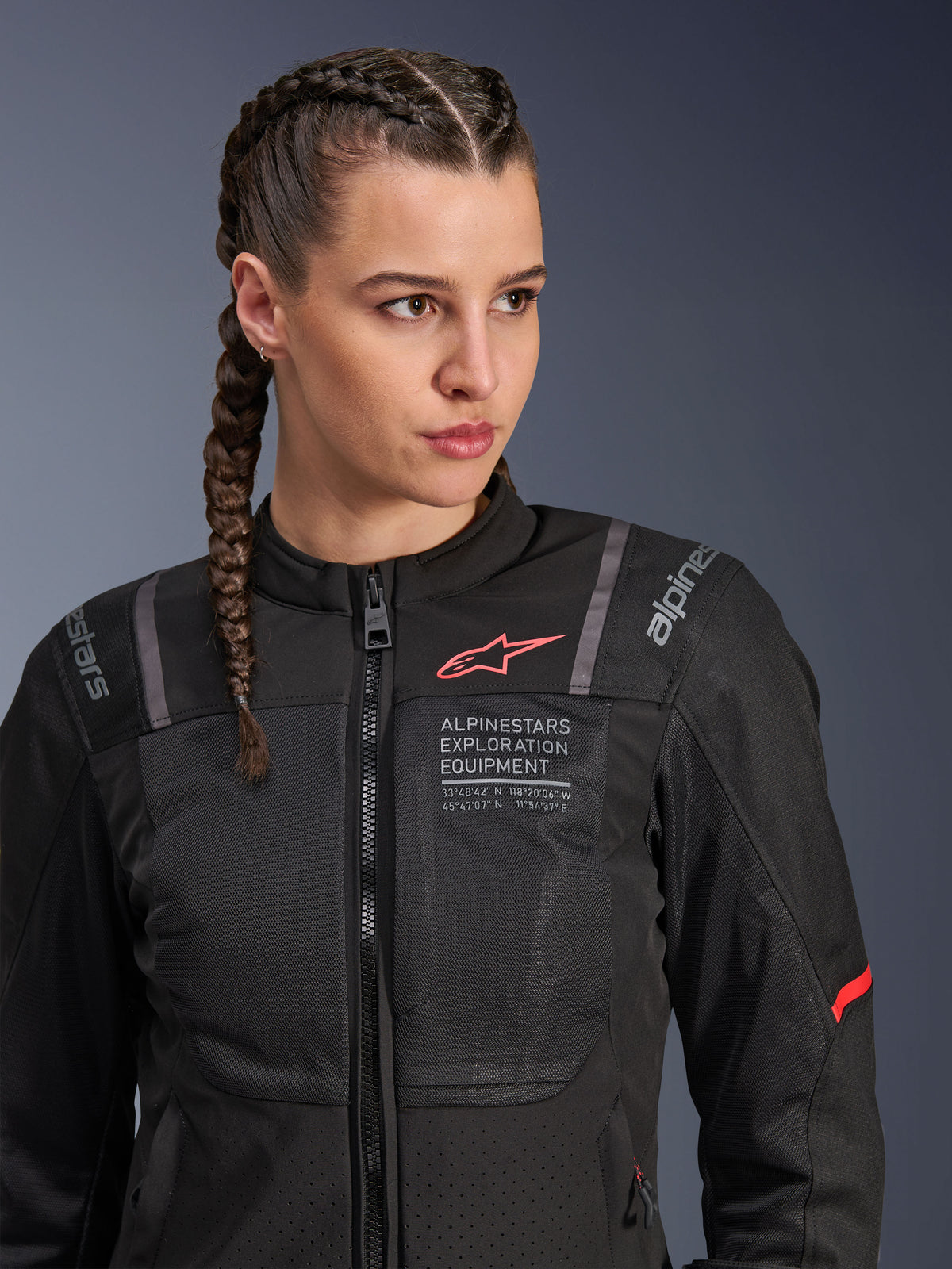 Alpinestars Stella ST-2 Air jakke, motorcykeljakke til kvinder i sort, med mesh-paneler for luftgennemstrømning, 'Alpinestars Exploration Equipment' branding med koordinater og rødt logo på brystet, båret af en model med flettet hår