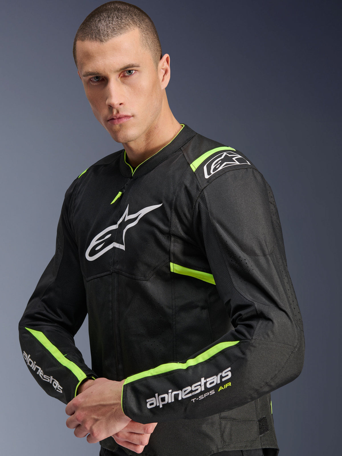 Alpinestars T-Sps Air V2-jakke, sort og gul fluo, tekstil-motorcykeljakke båret af model, med tech mesh-paneler for luftgennemstrømning, hvidt Alpinestars-logo på brystet og gul fluo detaljer på skuldre og ærmer.