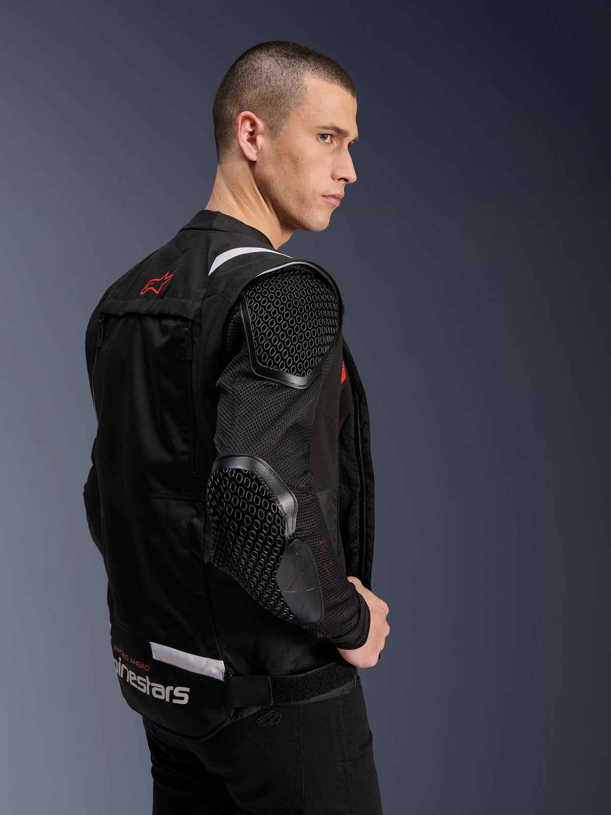 Alpinestars T-Stunt Air jakke, motorcykeljakke, sort, sideprofil af en model iført jakken med sportssnit, mesh-ærmer og synlig bikubemønstret beskyttelse på skulder og albue, rødt logo på ryggen, hvid branding ved taljen.