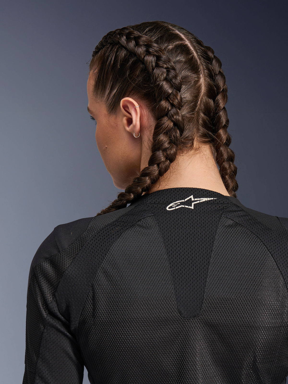 Alpinestars Woman Stella Troop-Air Jakke, sort, detaljeret visning af øvre ryg og nakke bagfra, kvinde med franske fletninger, hvidt Astars-logo på kraven, letvægts 2D tech-mesh-stof til ventilation