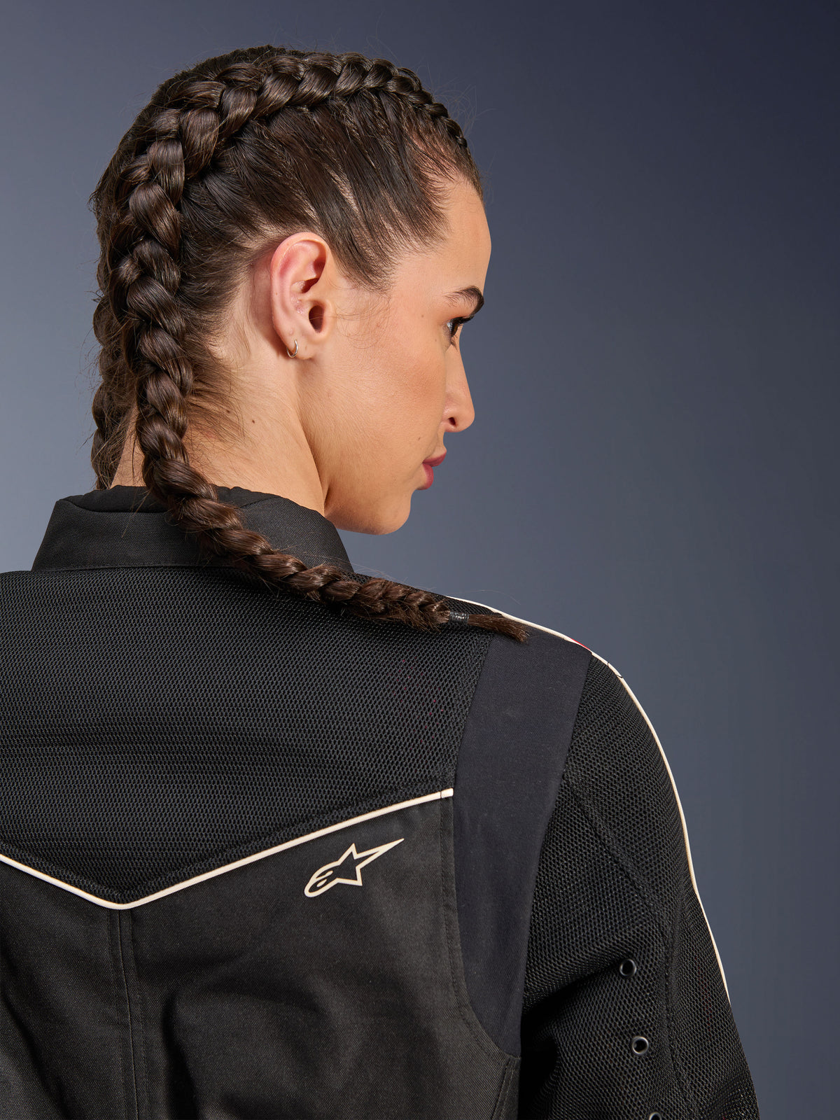 Kvinde iført Alpinestars Stella T-Dyno Air-jakke, nærbillede bagfra med fokus på skuldre og bærestykke, sort med åndbare 3D-mesh-paneler, hvid piping og lille Astars-logo, model med flettet hår, urbant motorcykeltøj
