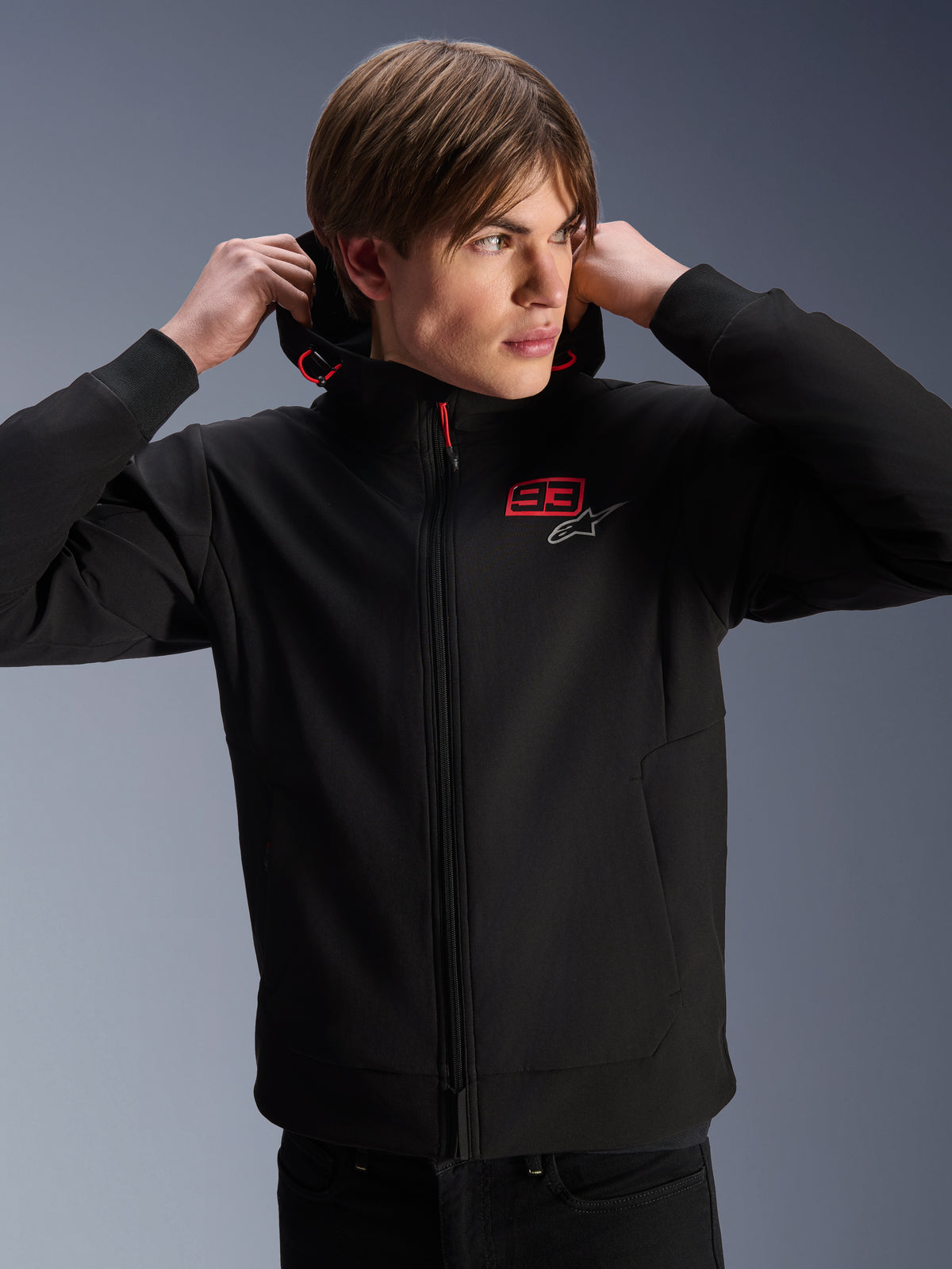 Alpinestars MM93 Radium Tech Hoodie, urban motorcykeljakke, sort med røde og sølvfarvede logoer, båret af en mandlig model, har gennemgående lynlås og ribbede manchetter, afslappet lifestyle motorsportbeklædning