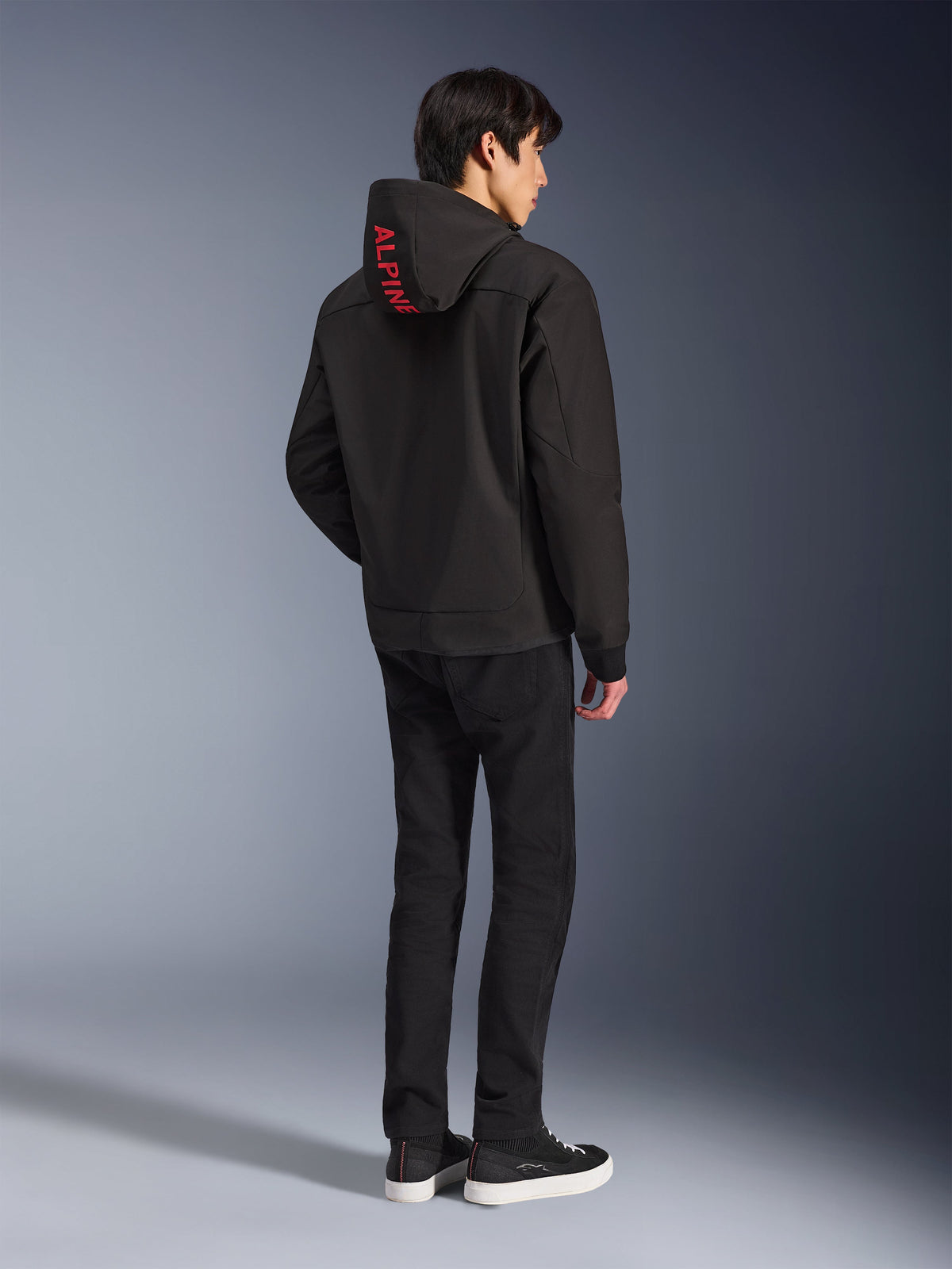 Alpinestars Radium Tech Hoodie, sort med rød Alpinestars-branding på hætten, set bagfra på en mandlig model, båret med sorte bukser og sneakers, teknisk urbant køreudstyr