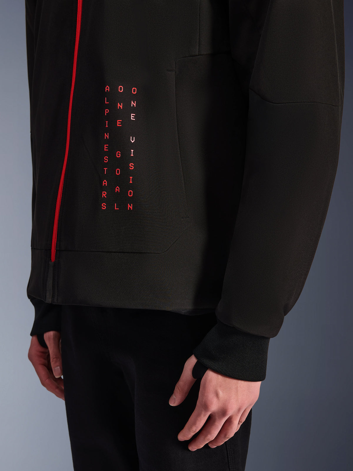Alpinestars Radium Tech Hoodie, urban motorcykeljakke, sort og klar rød, nærbillede af frontgrafik med lodret rød tekst 'ALPINESTARS ONE GOAL ONE VISION', rød lynlås og ribbet manchet med tommelfingerhul.