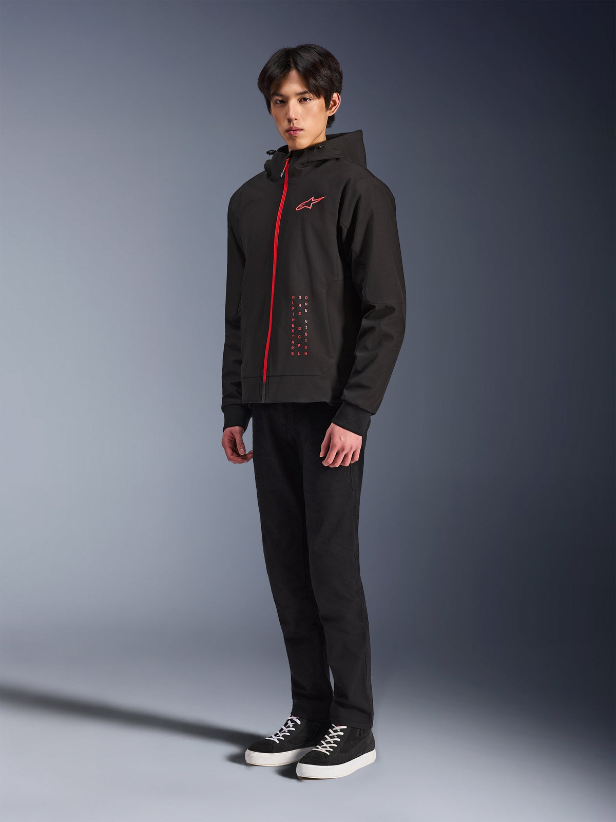 Alpinestars Radium Tech Hoodie, Black Bright Red, teknisk hættetrøje til bykørsel med rød lynlås foran og logo på brystet, båret af en model med sorte bukser og sorte sneakers med hvide såler, studiefoto i fuld figur