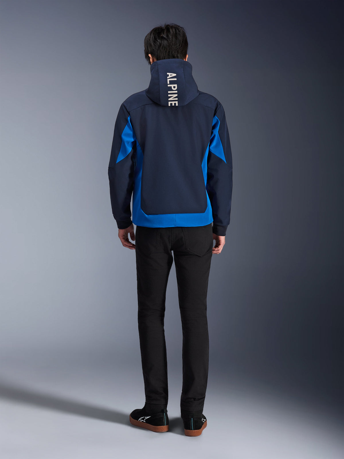 Alpinestars Radium Tech Hoodie, Night Navy og Royal Blue, set bagfra med vertikal 'ALPINE'-branding på hætten, kongeblå sidepaneler og kant, afslappet urban motorcykelhættetrøje med vindtæt 3L-skal, båret med sorte bukser