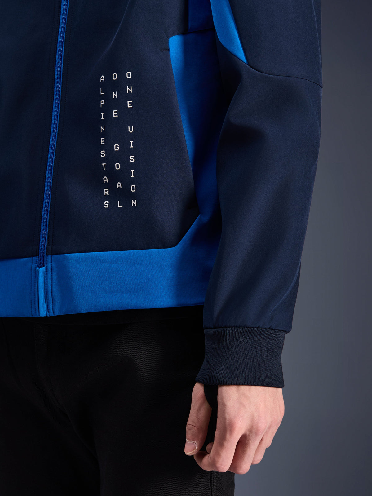 Alpinestars Radium Tech Hoodie, urban motorcykel-hættetrøje, Night Navy og Royal Blue, nærbillede af sidepanel med hvid vertikal tekstgrafik, ribstrikket stretch-manchet og blå lynlåslukning