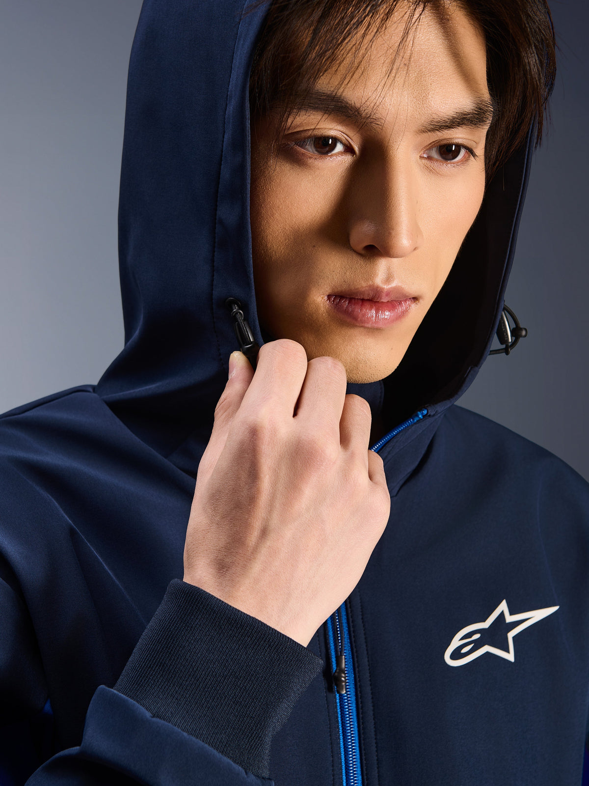 Alpinestars Radium Tech Hoodie, Night Navy Royal Blue, nærbillede af mand iført hættetrøje med hætten oppe, hvidt Astars-logo på brystet, blå lynlås, urban teknisk kørejakke