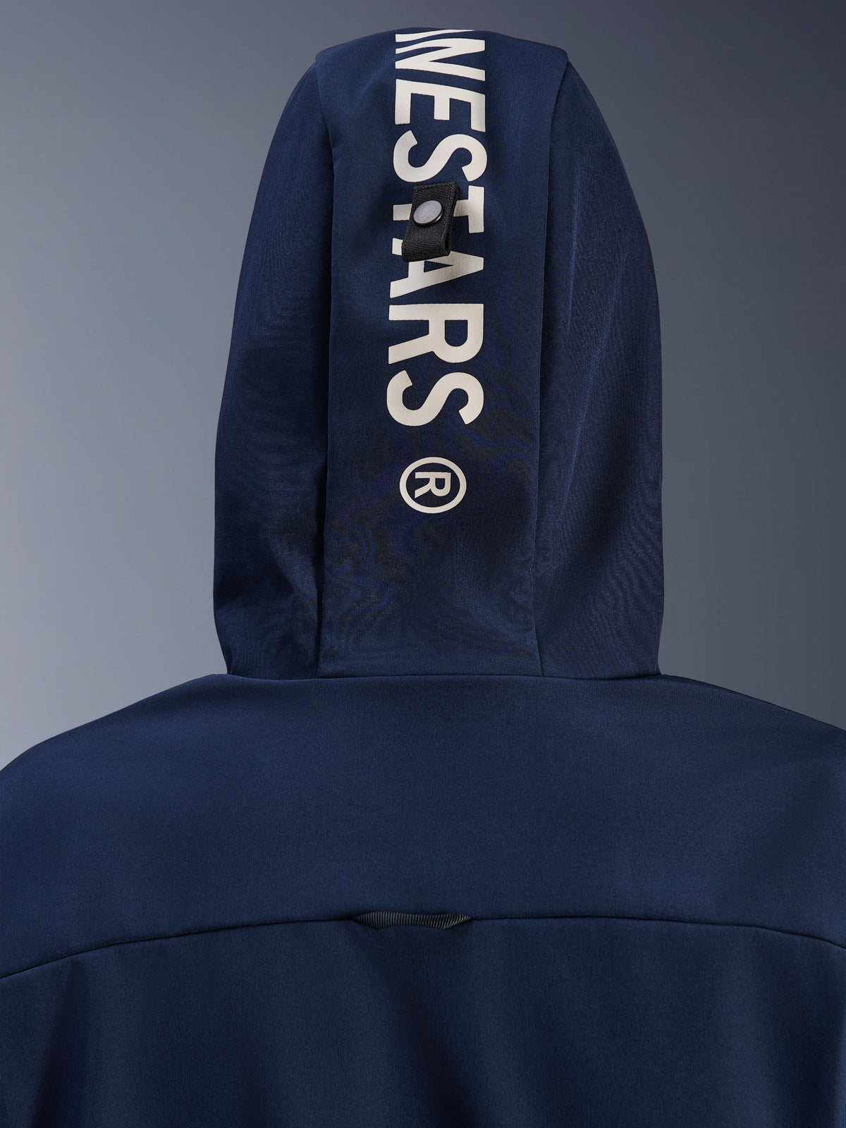 Alpinestars Radium Tech Hoodie i Night Navy Royal Blue, nærbillede af hætten bagfra med lodret hvid Alpinestars-branding og et sikkert løkke-fastgørelsessystem, teknisk motorcykelbeklædning til bykørsel.