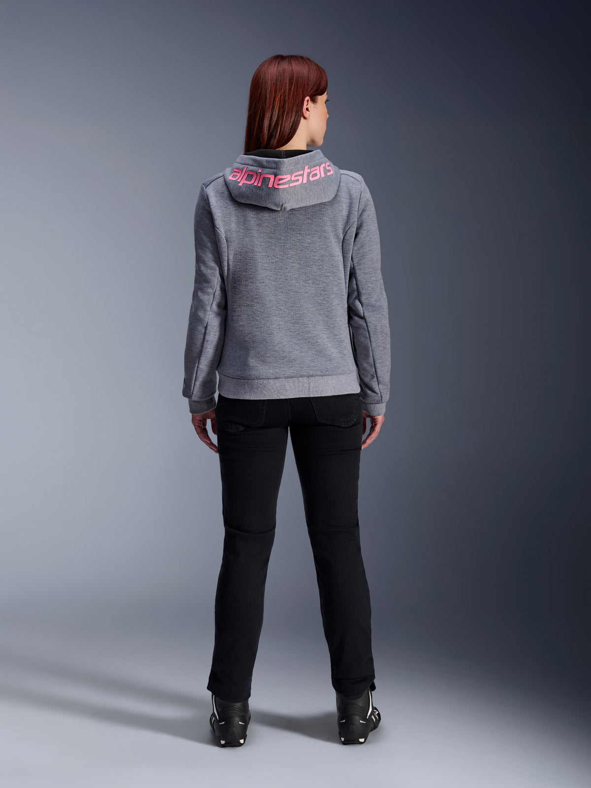 Alpinestars Stella Chrome V2 Sport Hoodie, motorcykelhættetrøje til kvinder, Gray Heather og Pink Fluo, set bagfra viser lyserødt Alpinestars-logo på hætten, båret med sorte kørebukser og støvler, afslappet motorcykelbeklædning til kvinder