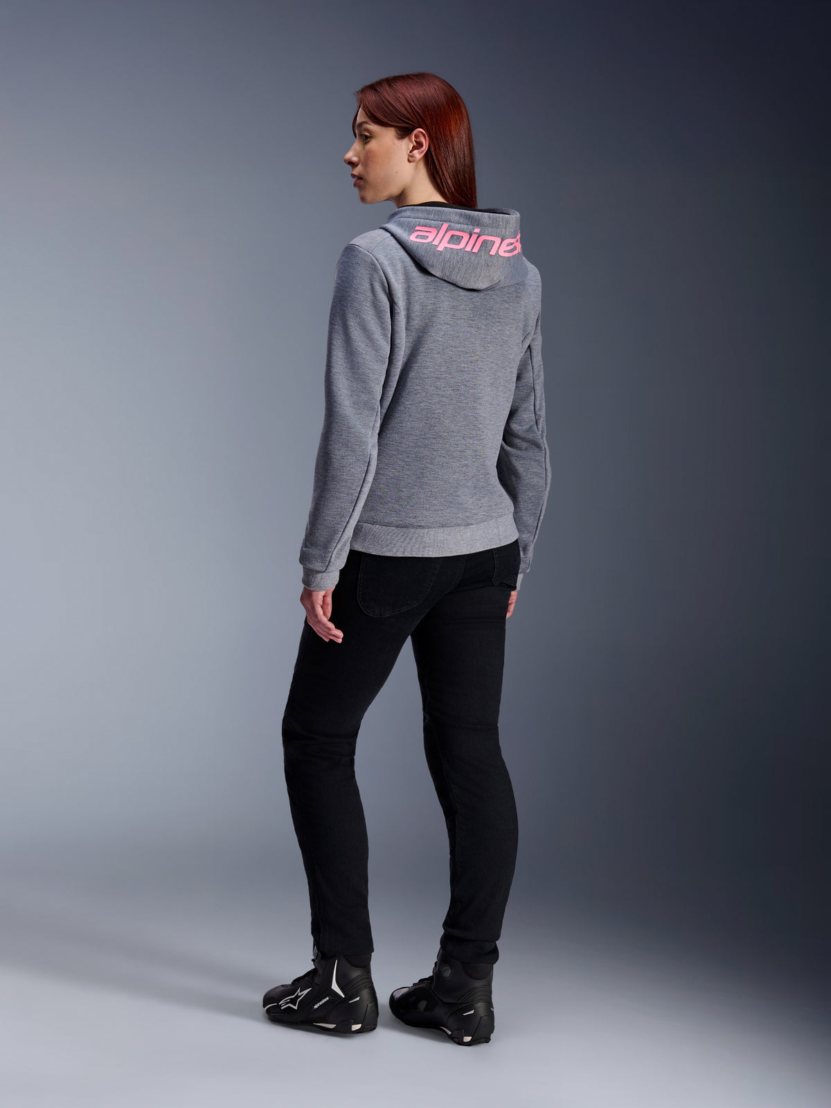 Alpinestars Stella Chrome V2 Sport Hoodie, motorcykelhættetrøje til damer, gråmeleret med Pink Fluo-branding på hætten, set bagfra, båret med sorte bukser og køresko, afslappet urban street-stil med motorcykelbeskyttelse