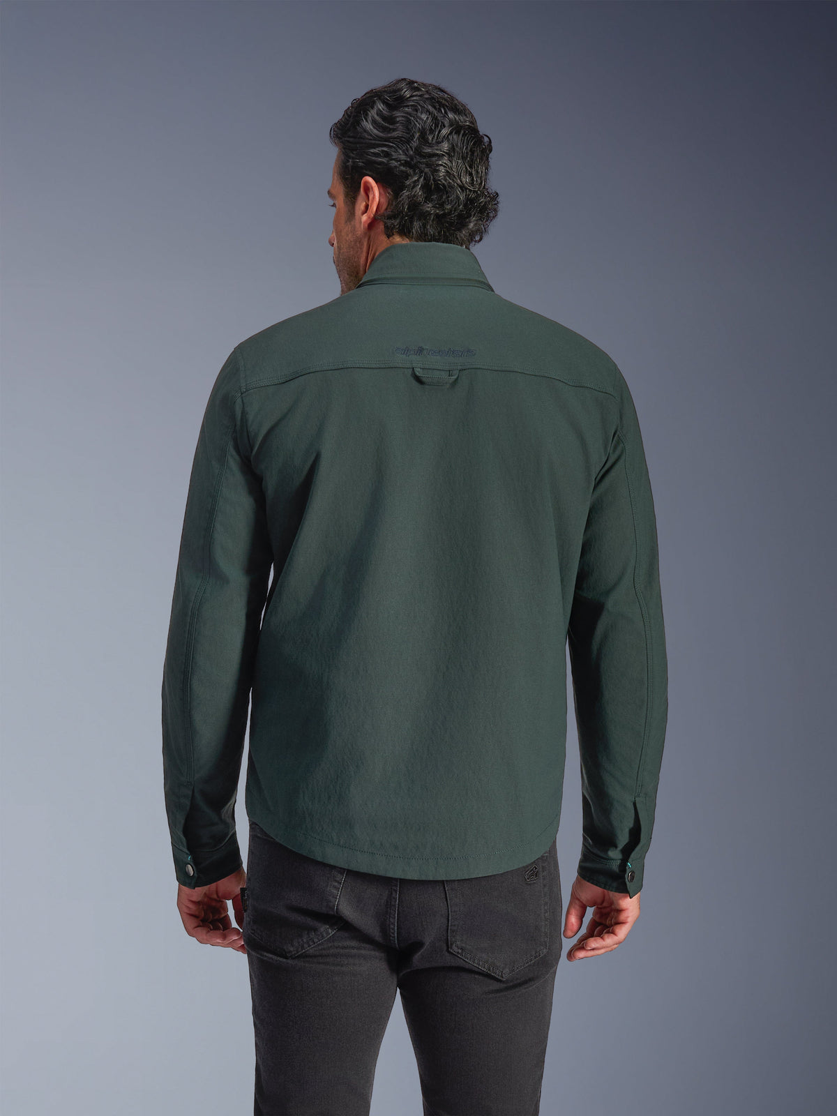 Alpinestars Bryon Water Resistant Overshirt, Dark Emerald green, rear view on model, embroidered logo on the upper back, durable waxed canvas, urban motorcycle riding jacket paired with dark pants