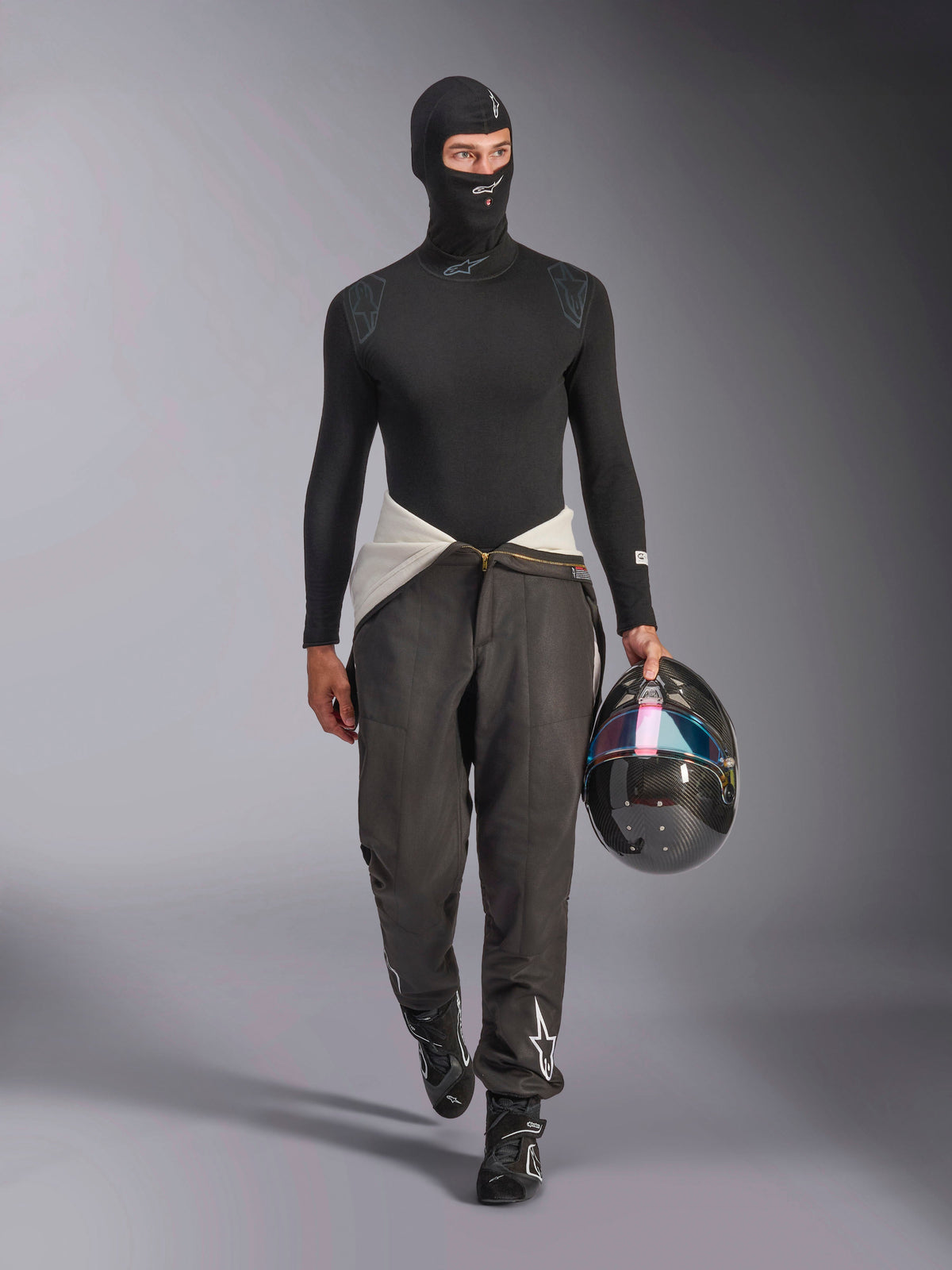 Alpinestars ZX Evo V3 Balaclava, sort, båret af en model i et komplet base layer-sæt med en matchende langærmet overdel og grå racerbukser, holder en kulfiberhjelm med et iriserende visir, professionelt racingudstyr
